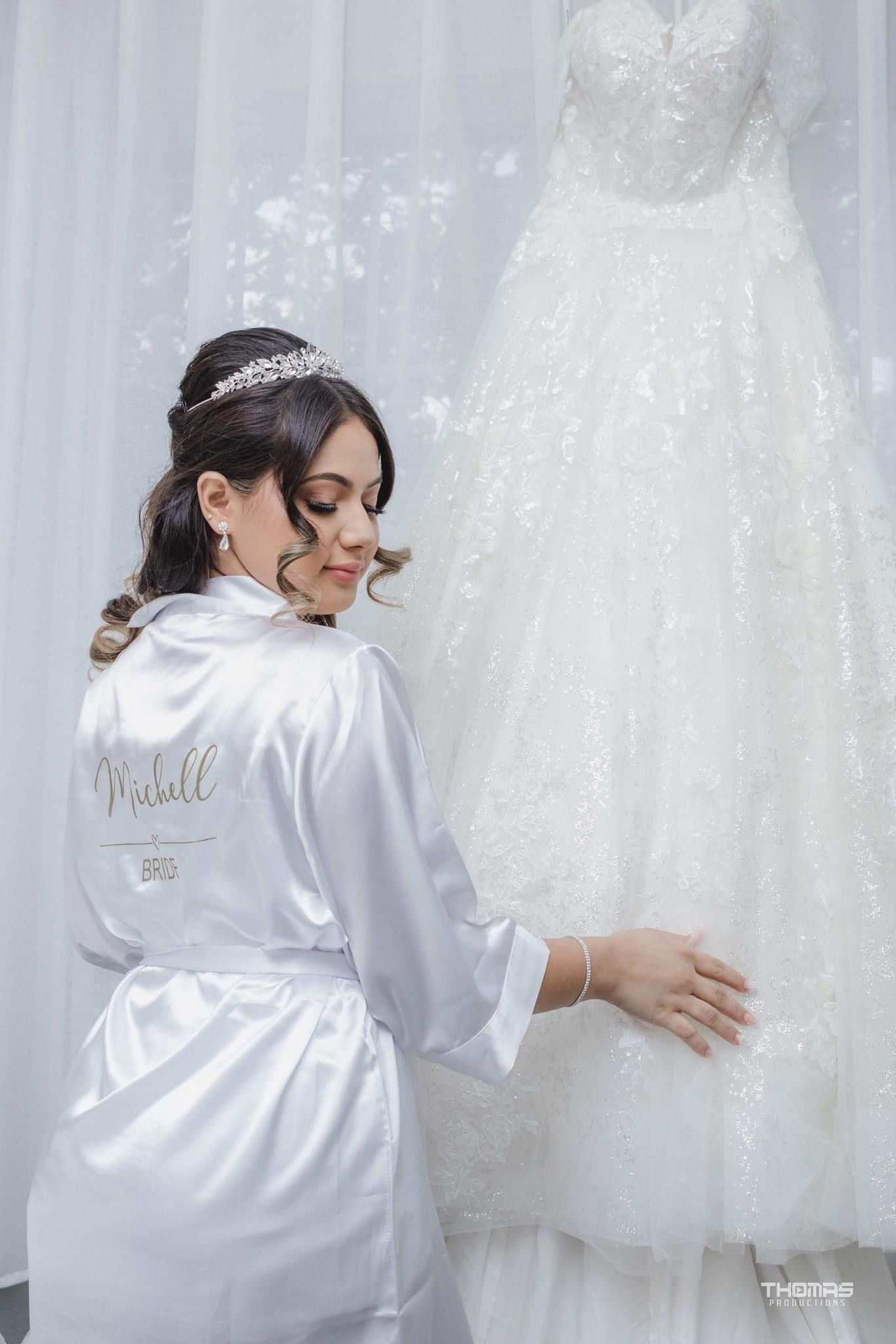 A white satin robe with personalized text is displayed against wedding dresses.