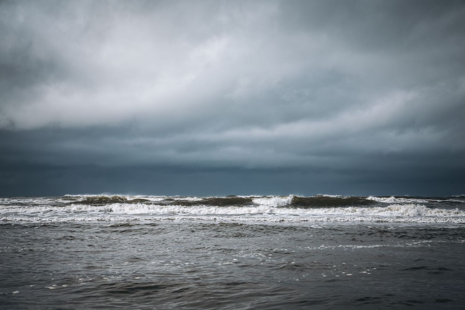 Dark stormy ocean waves crash under a dramatic overcast sky on a moody beach.