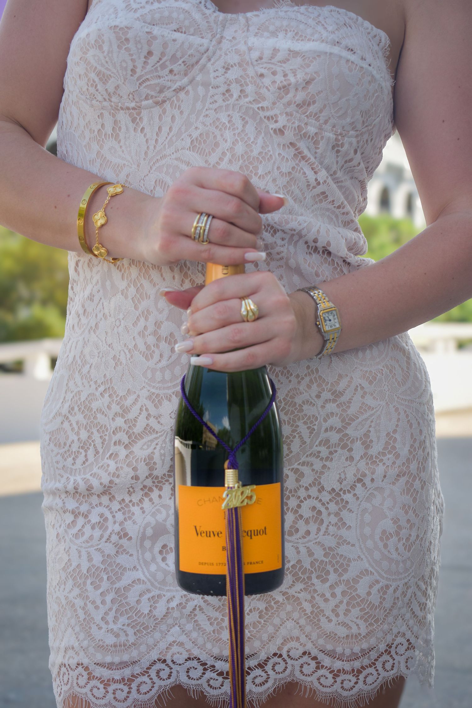 Close-up of woman in white lace dress holding Veuve Clicquot champagne bottle with gold jewelry.