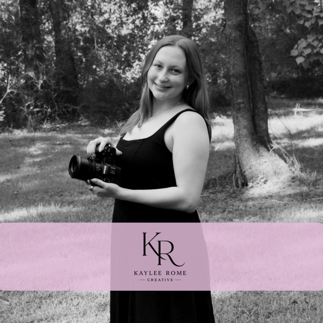 Smiling woman in a black dress holds a camera in a wooded park in black and white, with a Kaylee Rome Creative logo banner.
