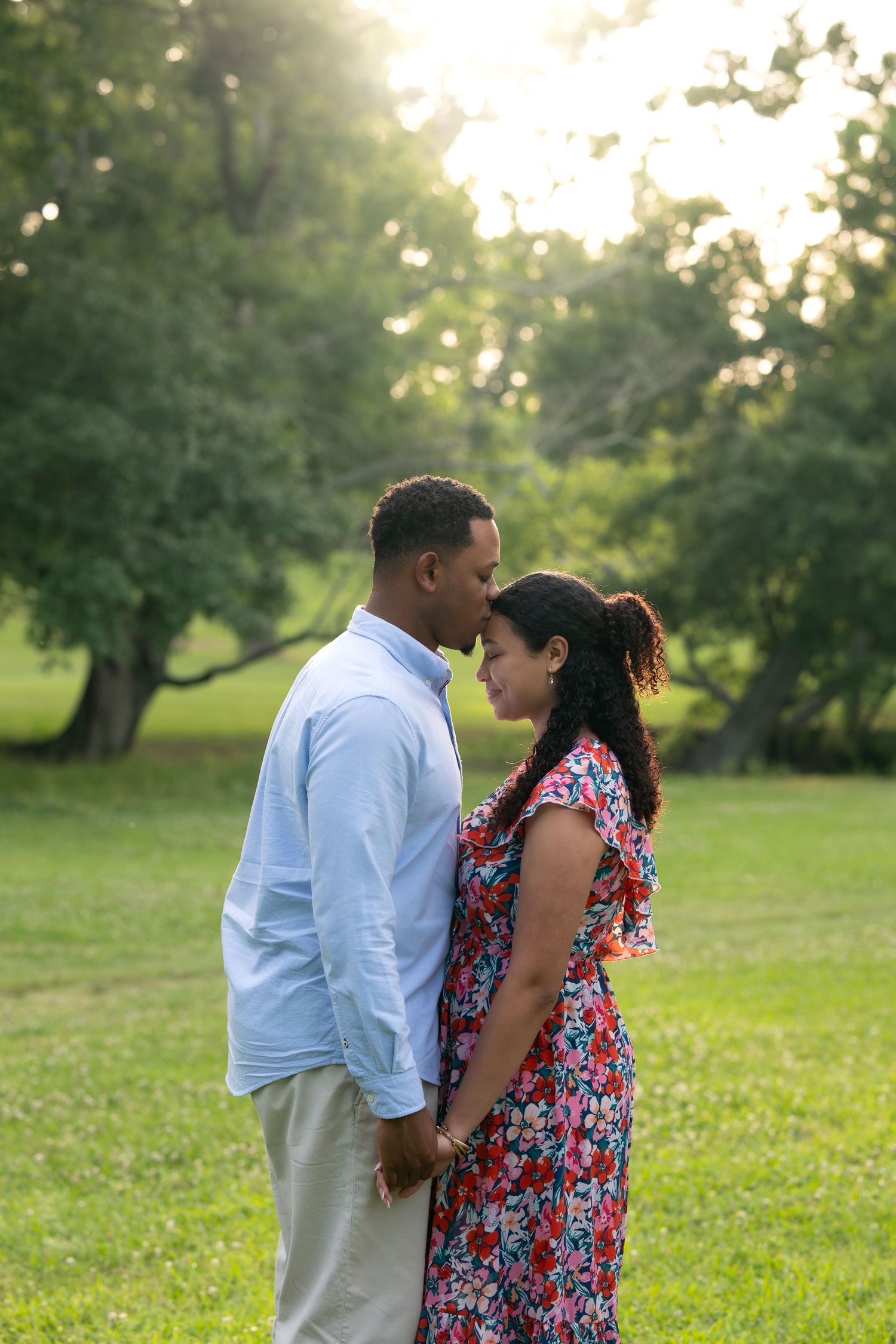 Romantic couple holding hands and gazing at each other in a lush green park at golden hour.