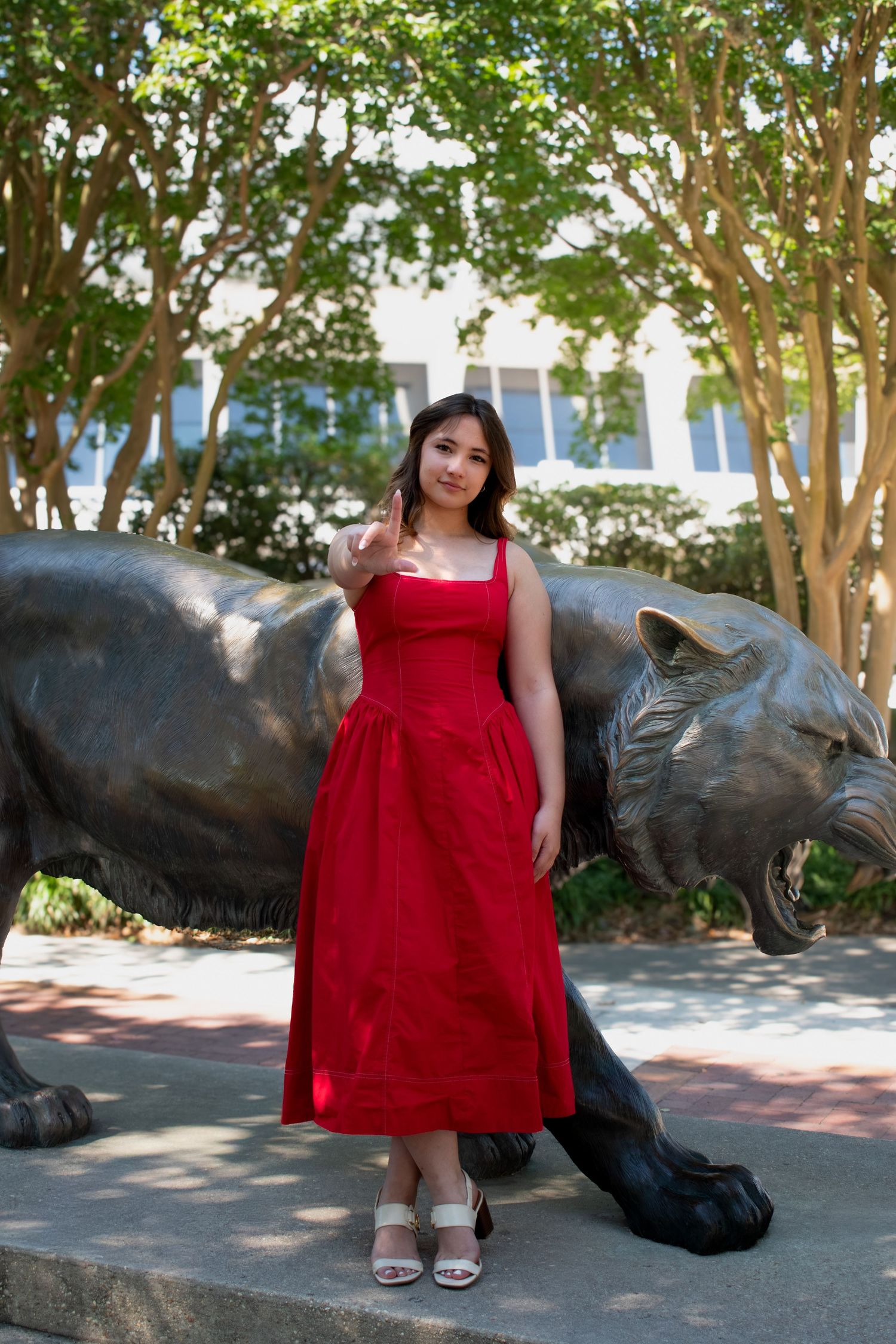Young woman in red midi dress posing beside a bronze panther statue outdoors on a sunny day.