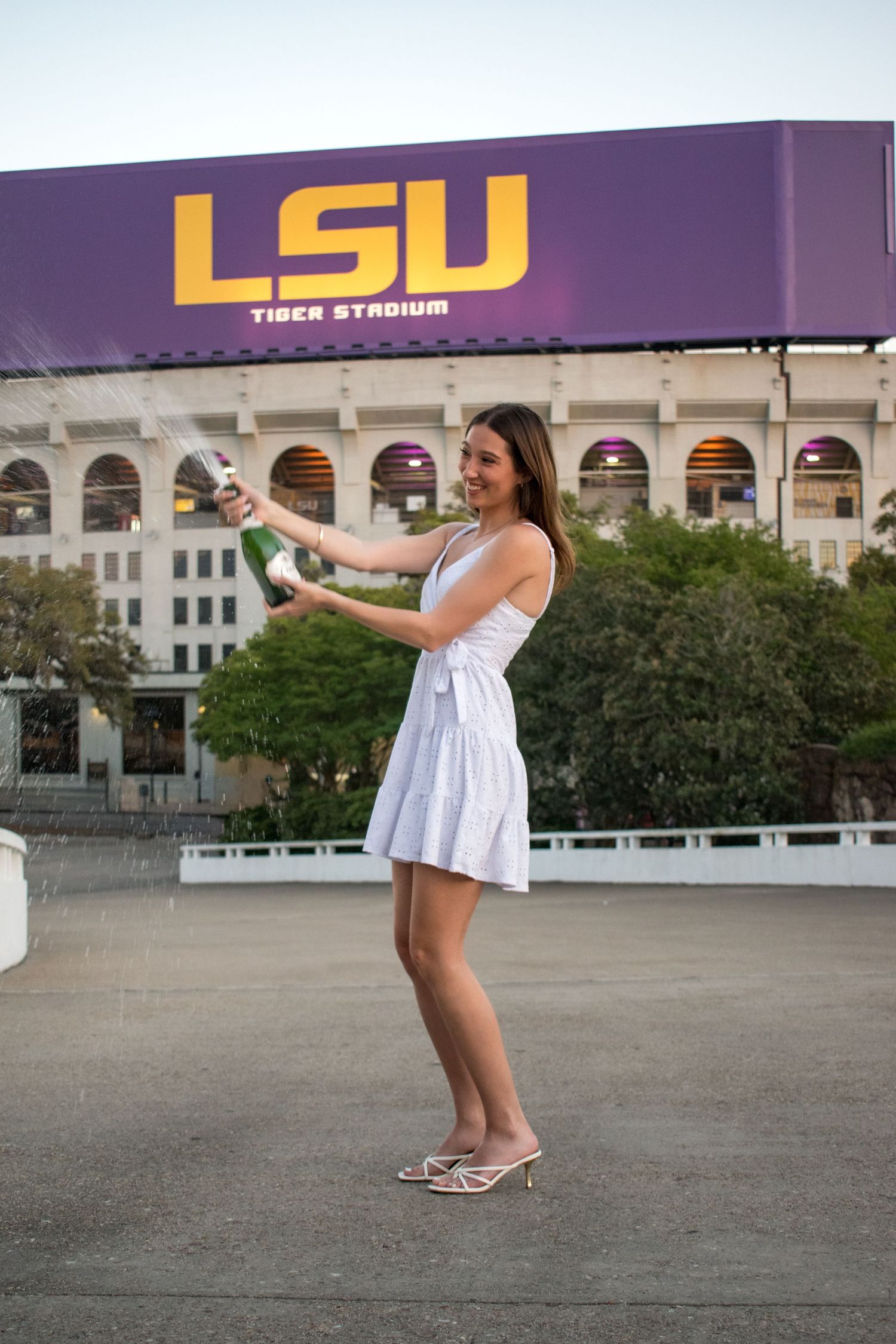 Woman in white dress popping champagne bottle outside LSU Tiger Stadium in Baton Rouge, Louisiana.