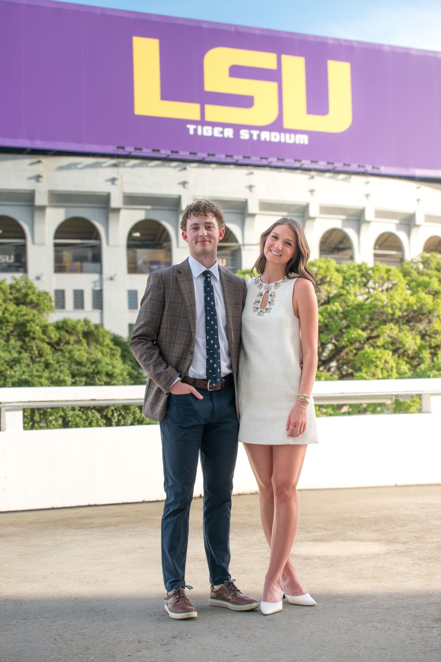 Couple poses together in front of LSU Tiger Stadium on a sunny day.