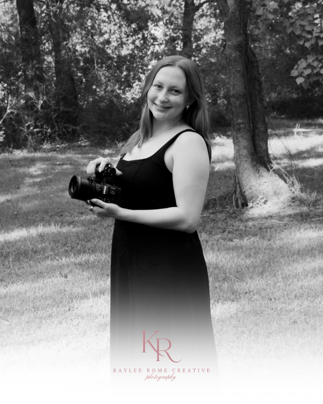 Woman in black dress holding camera outdoors, black and white portrait photo by Kaylee Rome Creative Photography.