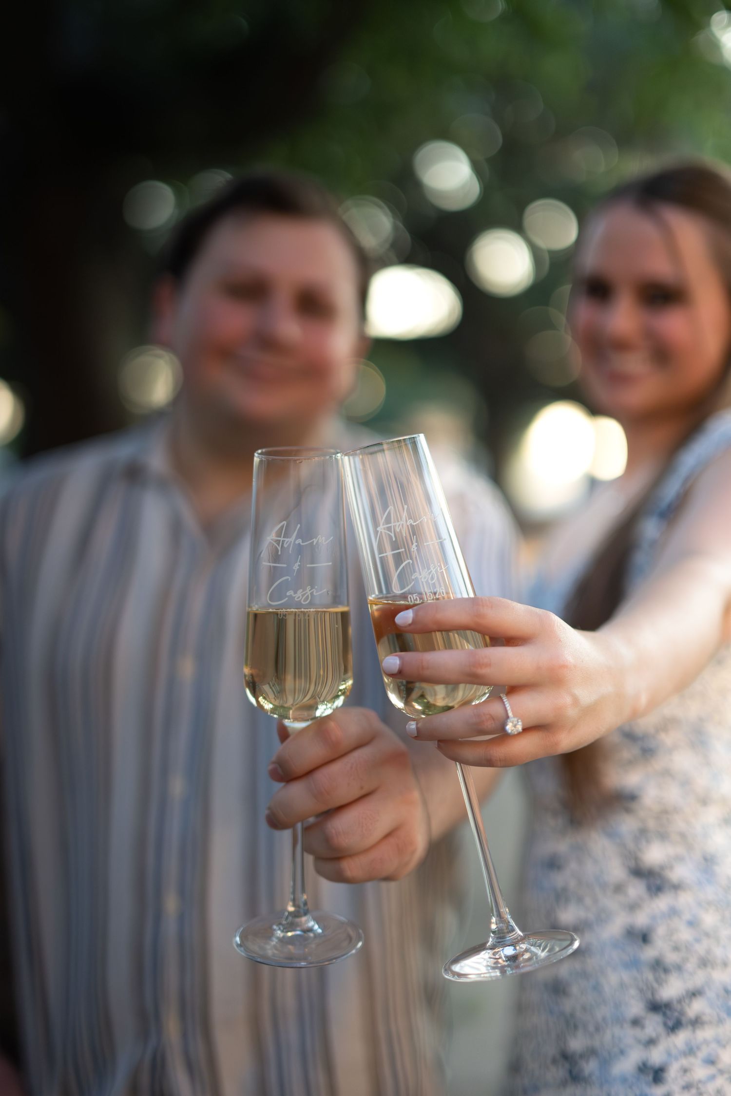 Couple toasting with engraved champagne flutes outdoors, celebrating a special occasion together.