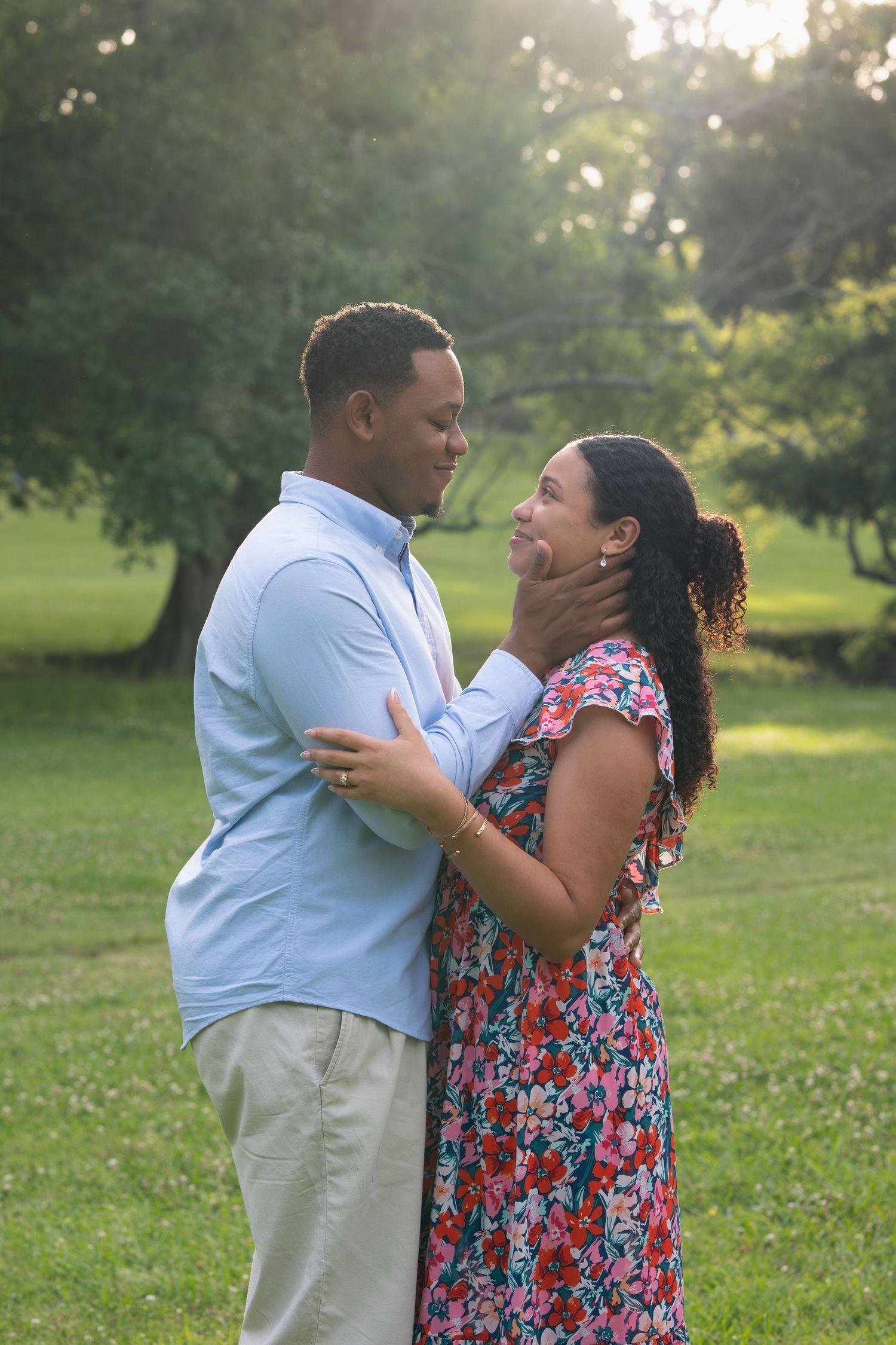 Loving couple standing close in a park, man gently cupping womans face while gazing into her eyes.