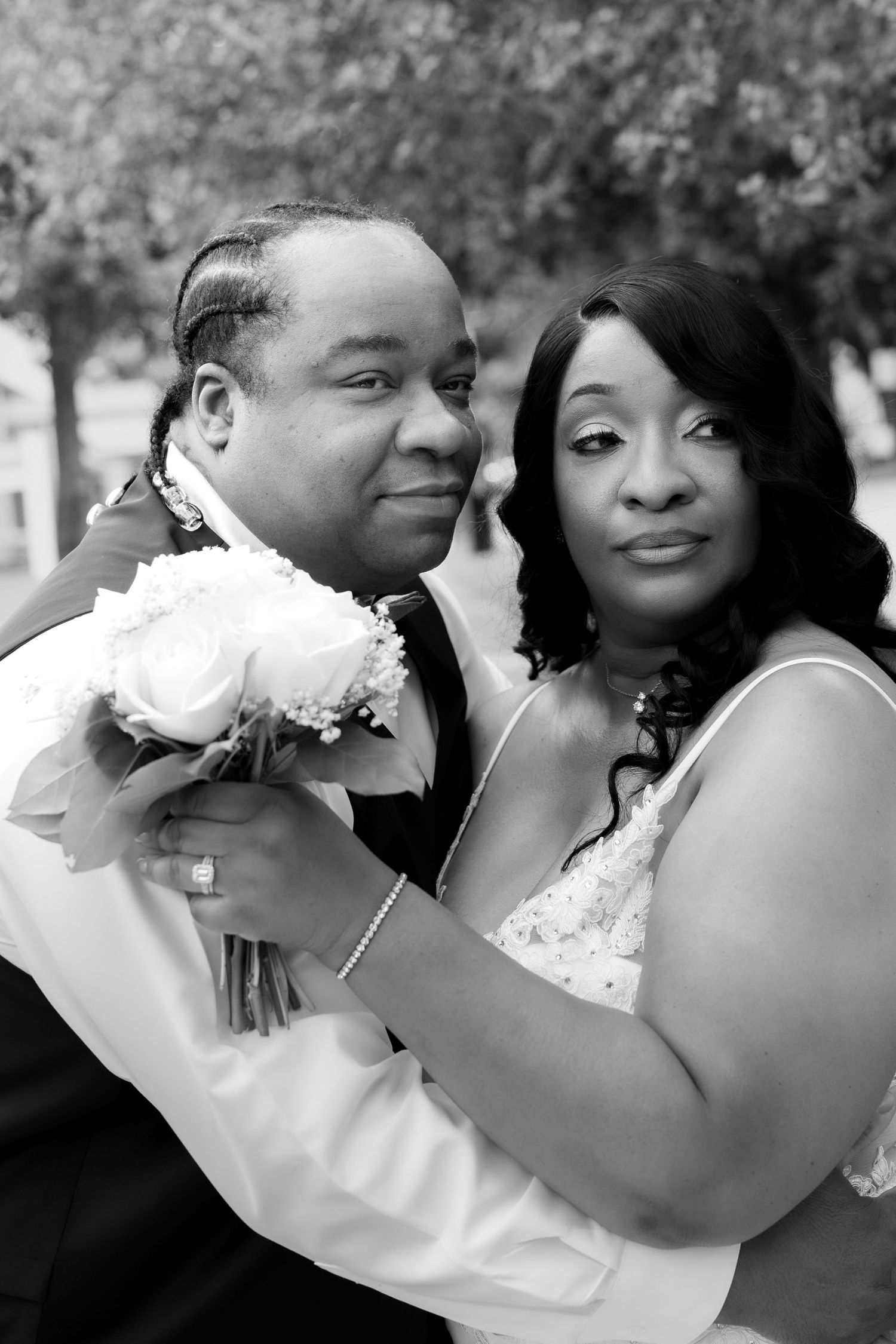 Black and white wedding photo of a couple, bride in white dress holding bouquet, groom in suit, posing outdoors.