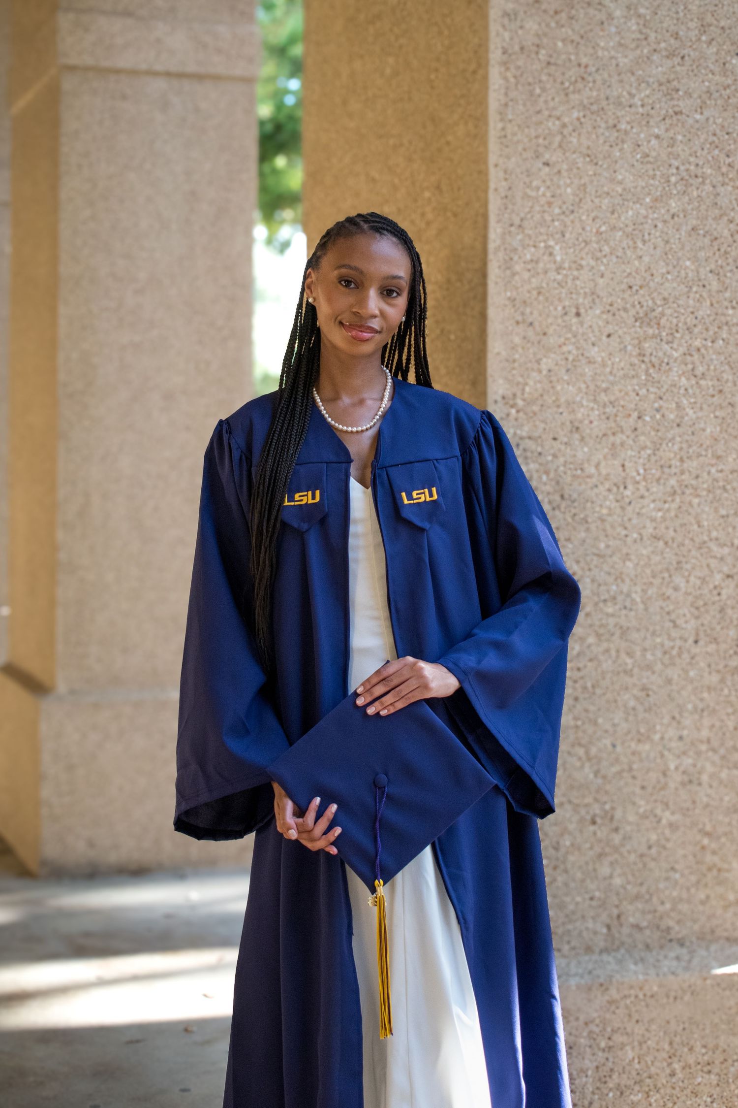 Young woman in LSU navy blue graduation gown and cap with gold tassel poses between stone columns.