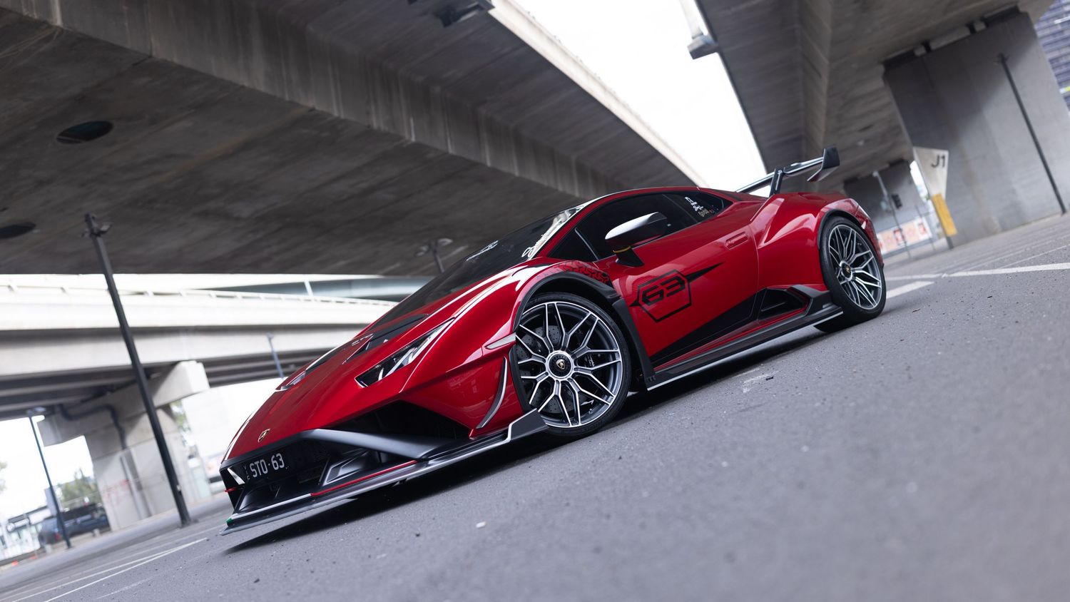 Red Lamborghini supercar with aggressive aerodynamic bodykit photographed from low angle under concrete bridge.