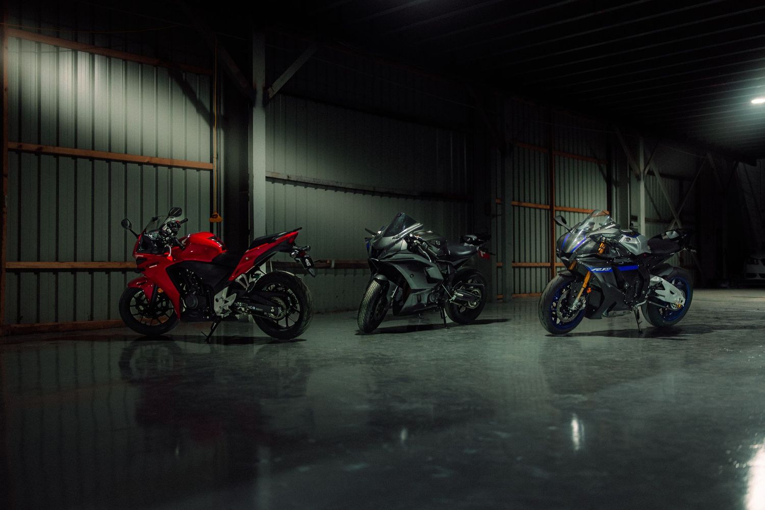 Three sport motorcycles in red, black, and blue parked inside a dimly lit garage showroom.