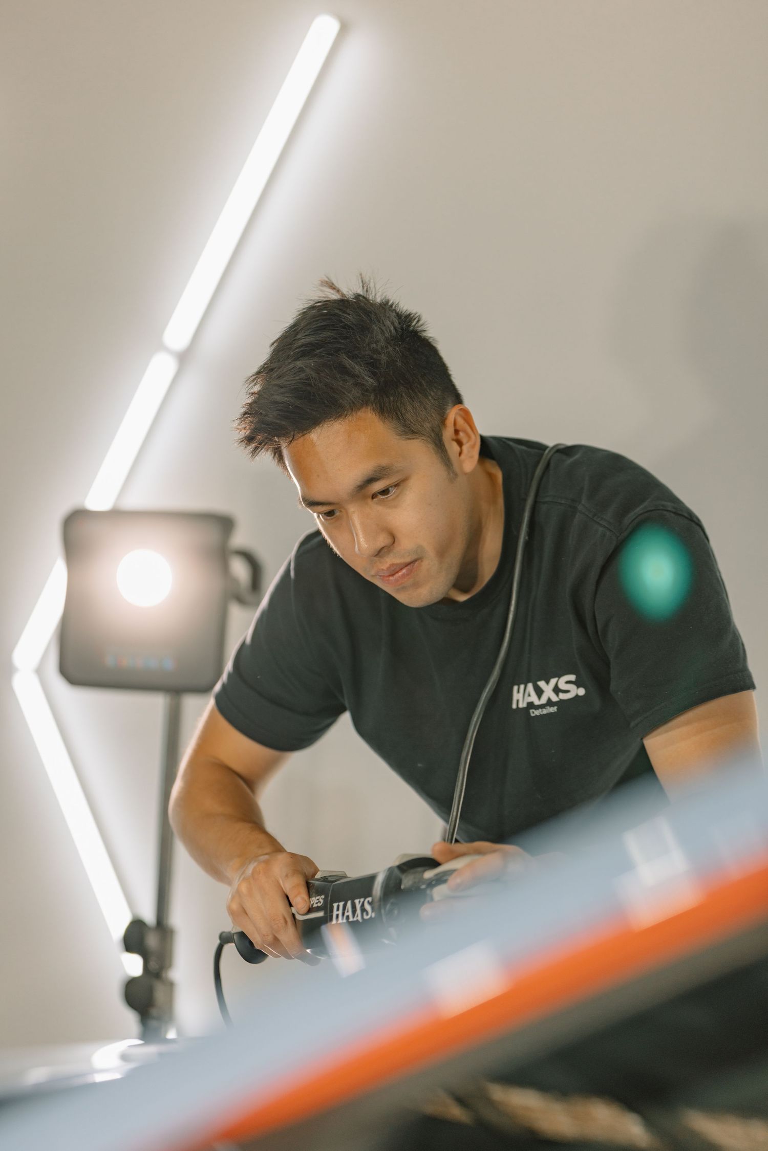 A focused auto detailer uses a  polishing machine on a car under bright studio lighting.