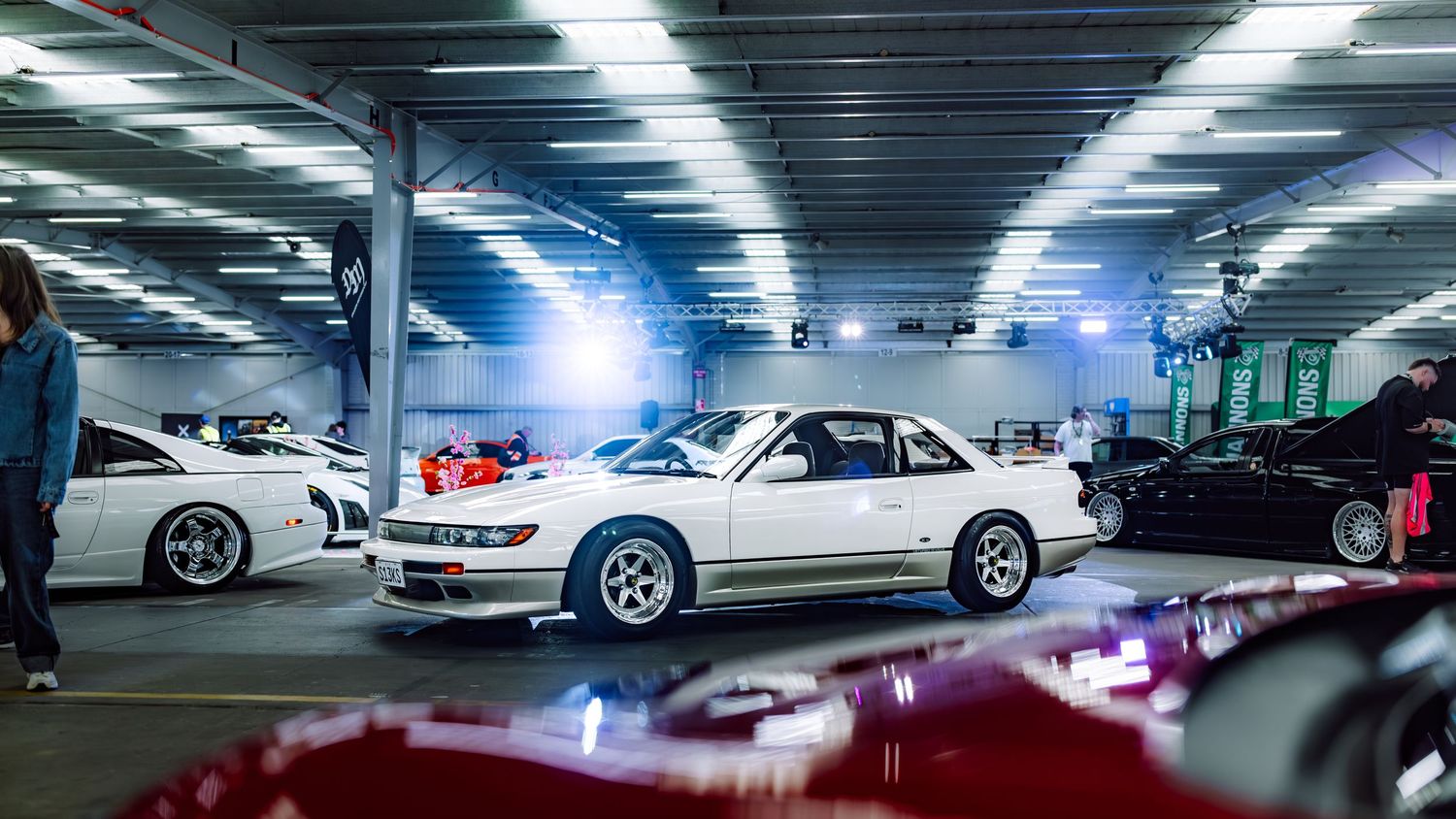 White classic Japanese sports cars displayed in an indoor automotive show garage with bright overhead lighting.