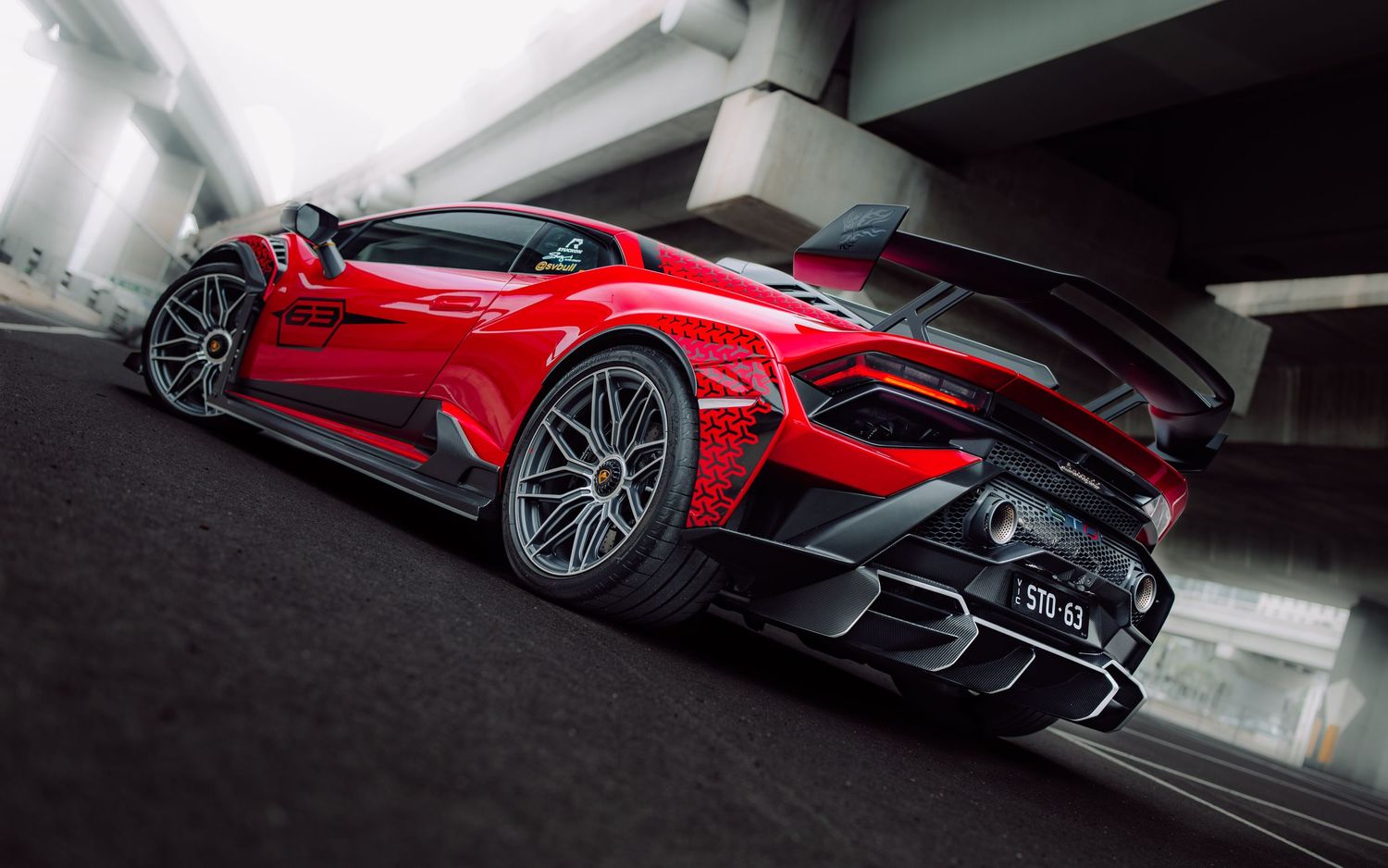 Red Lamborghini Huracan with large rear spoiler photographed from behind under a bridge.