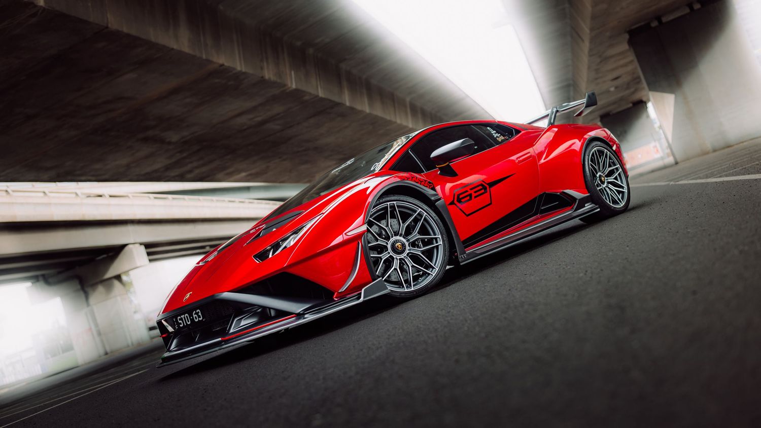 Red Lamborghini supercar speeding under a concrete bridge in a dramatic low-angle shot.