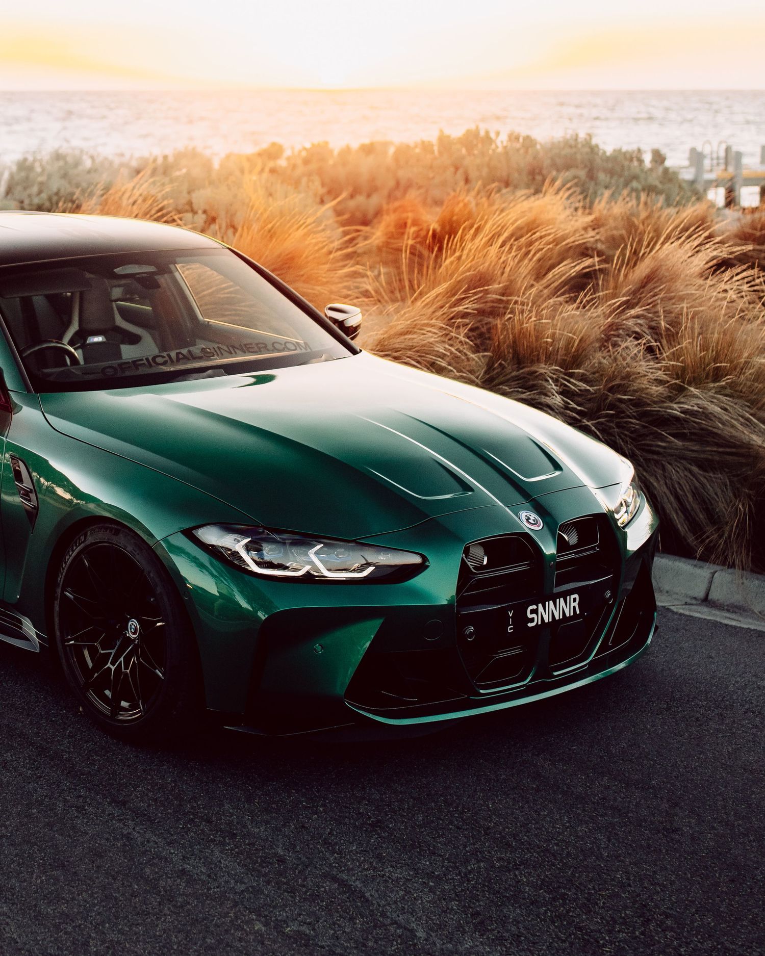 Green BMW M3 competition with aggressive front fascia photographed at golden hour.