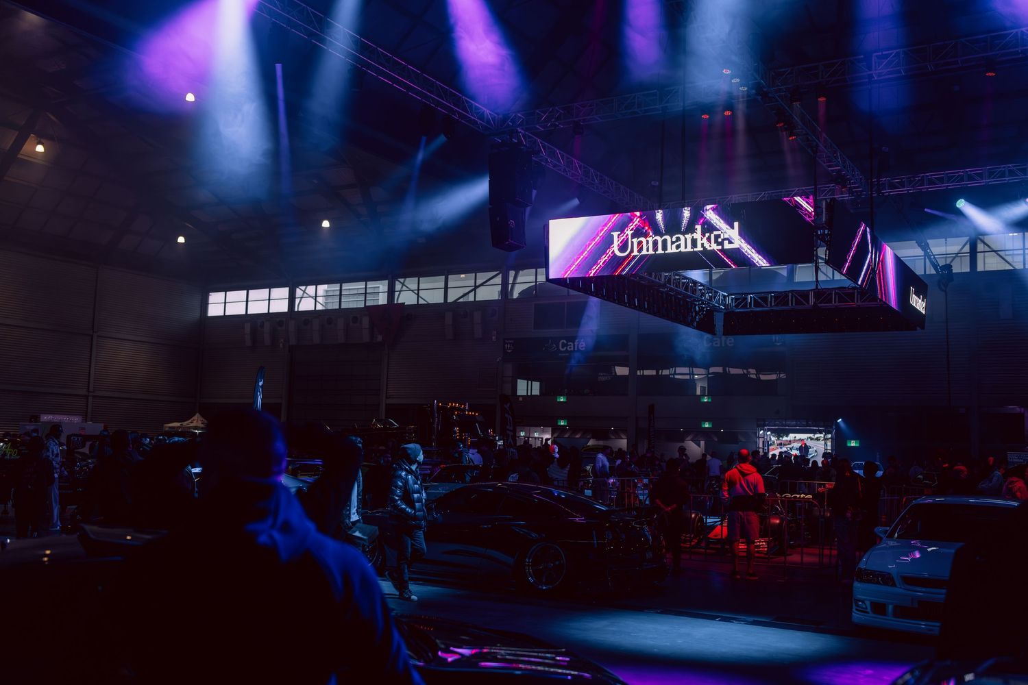 A dramatic indoor event venue with colorful stage lighting and an LED display screen illuminating a dark exhibition space.
