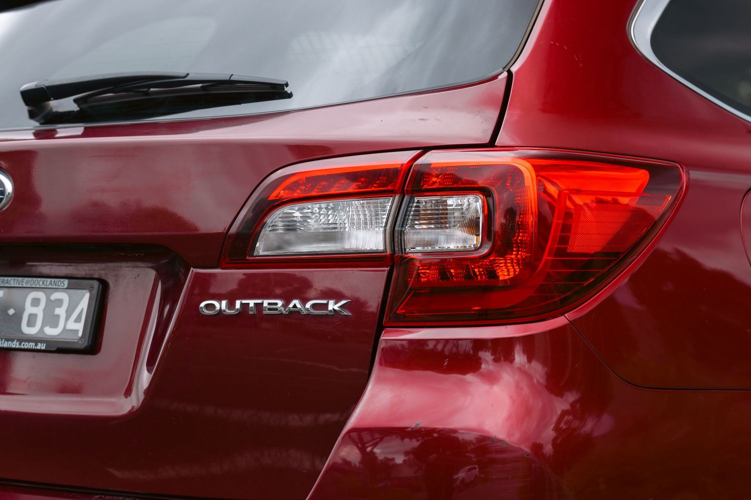 Close-up of a red Subaru Outback rear badge and tail light on a dark burgundy vehicle.