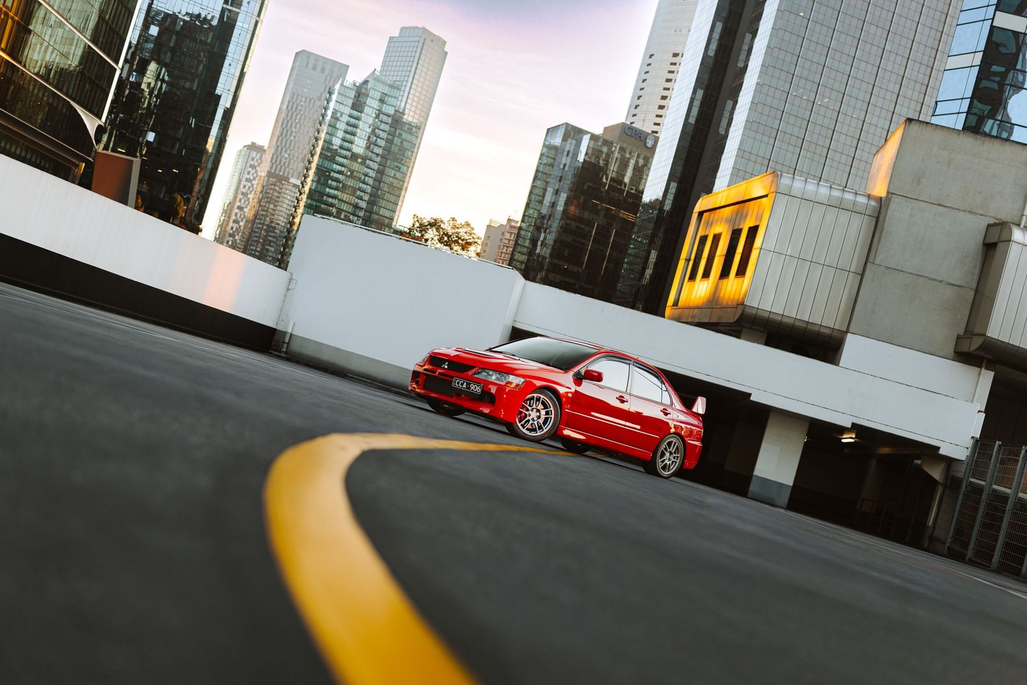 Red sports car parked on urban rooftop with city skyscrapers in background during golden hour.