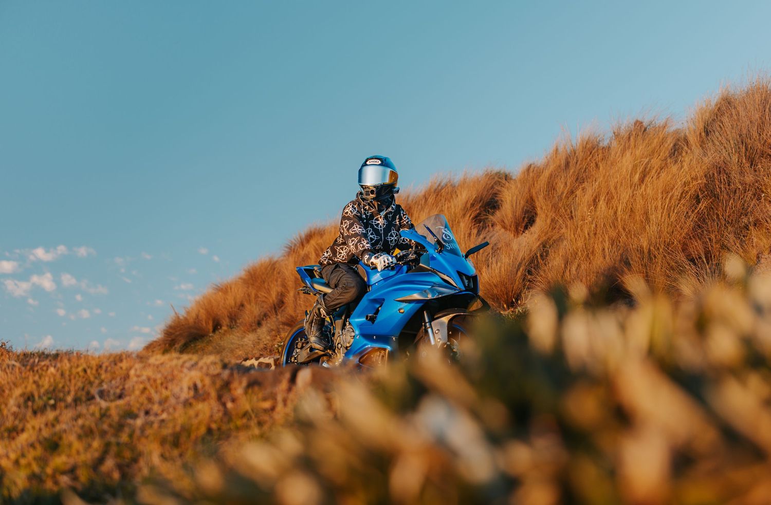 Rider on a blue motorcycle navigating a rugged hillside trail under clear blue sky.