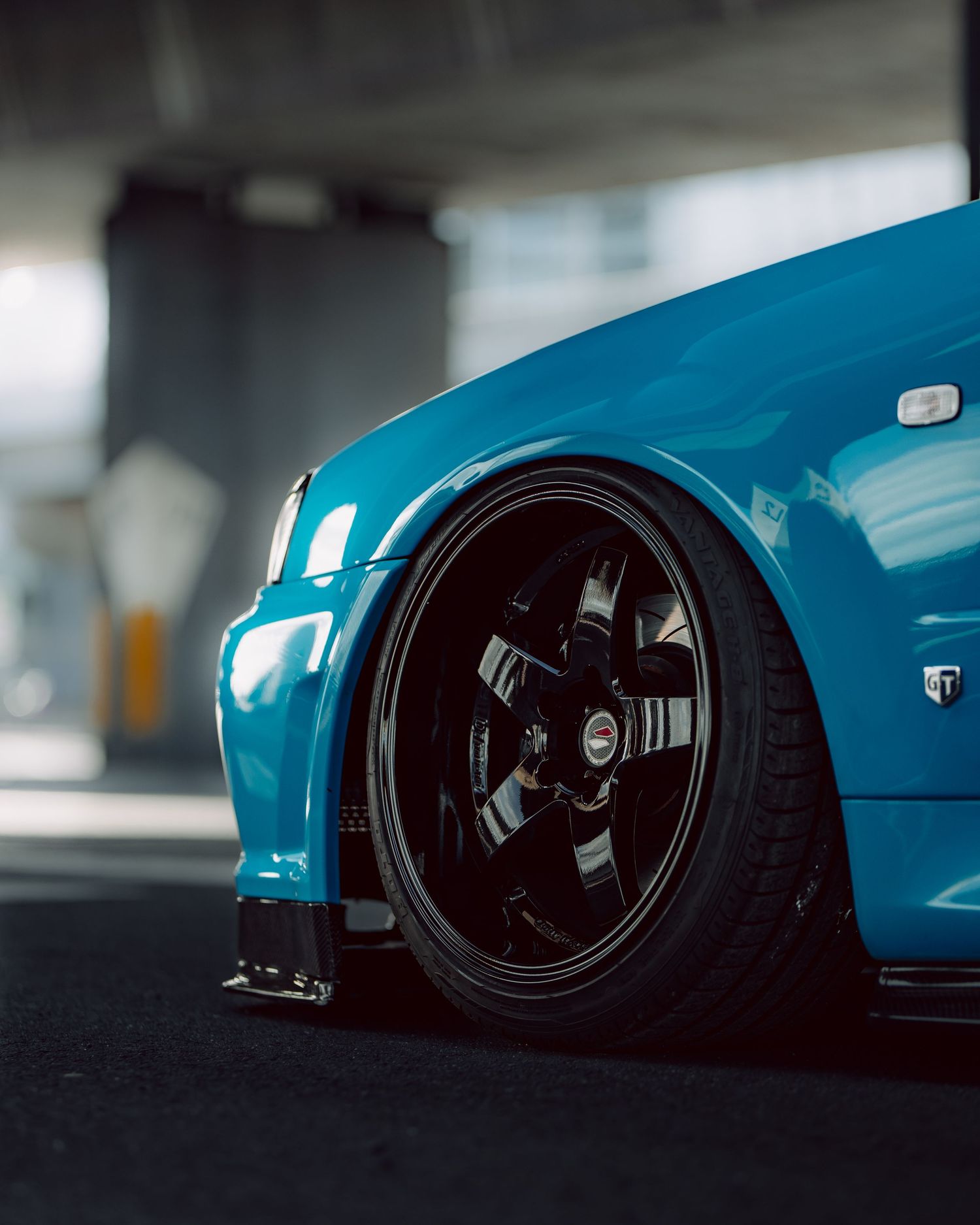 A lowered blue sports car with black aftermarket wheels parked in a garage, showcasing its aggressive stance.