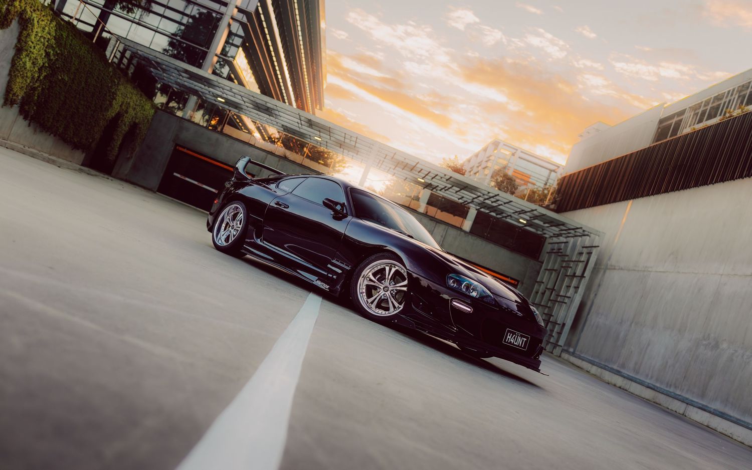 A dark purple Toyota Supra car parked on a road at sunset with warm golden light illuminating the scene.