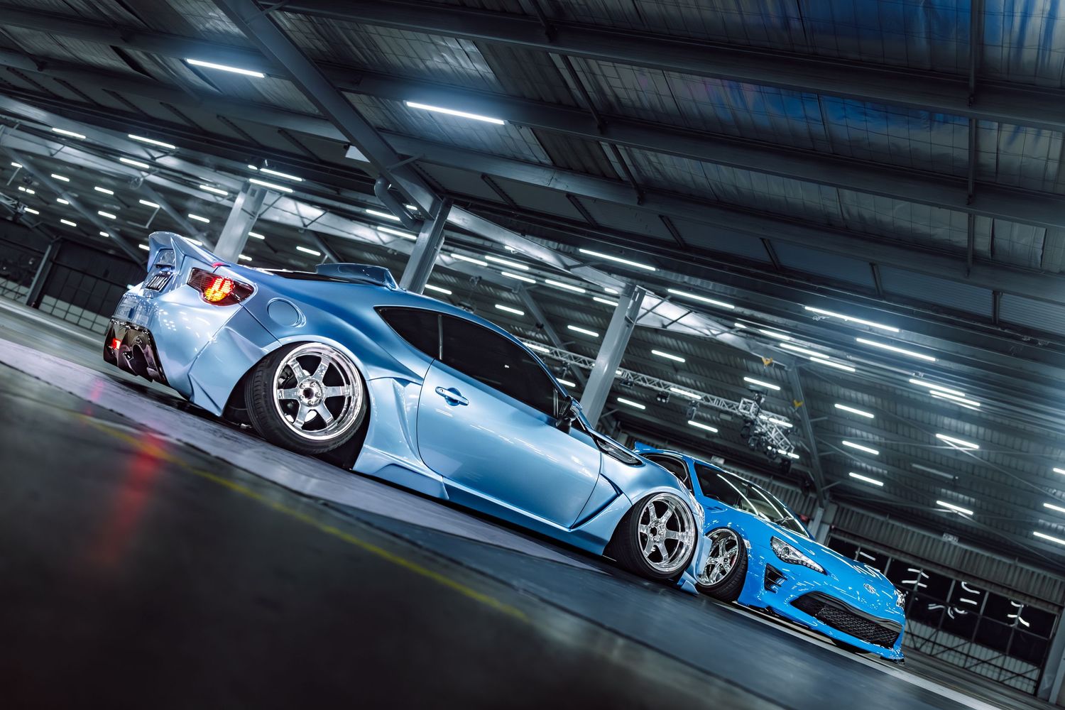 A modified baby blue sports car with wide body kit parked in a tunnel with bright overhead lighting.