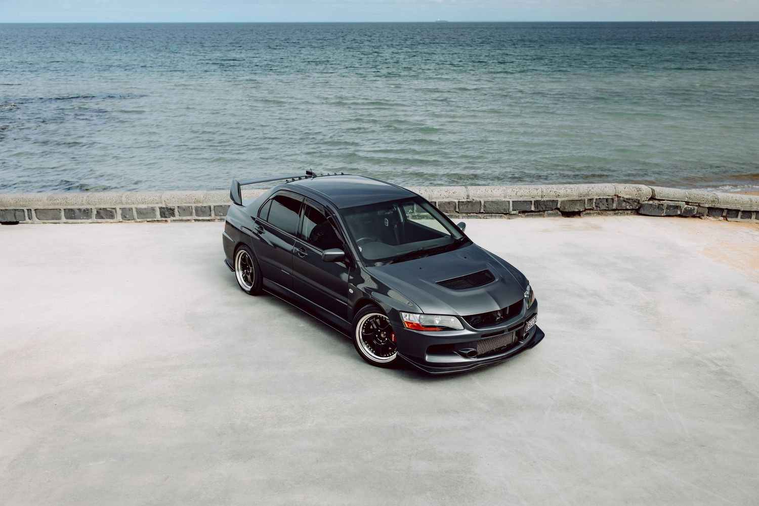 Black Mitsubishi Lancer Evolution parked near a seaside wall with ocean views in the background.