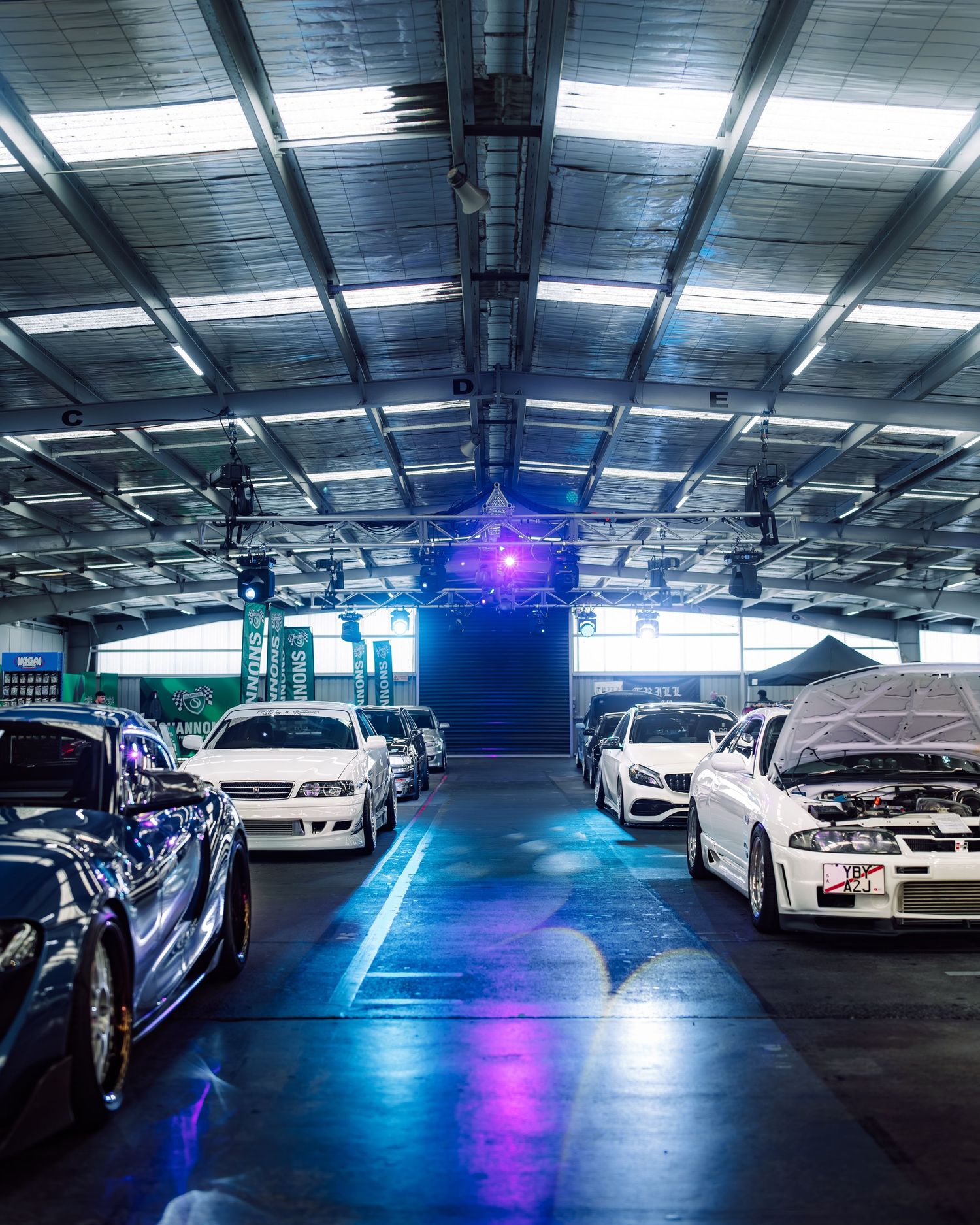 Cars displayed in a neon-lit indoor garage showroom with blue and pink lighting illuminating the sleek vehicles.