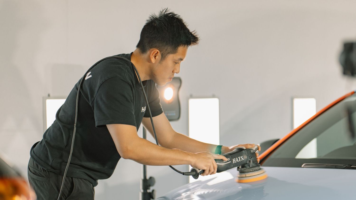 A man uses a RUPES orbital polisher on a car hood in a professional auto detailing studio.