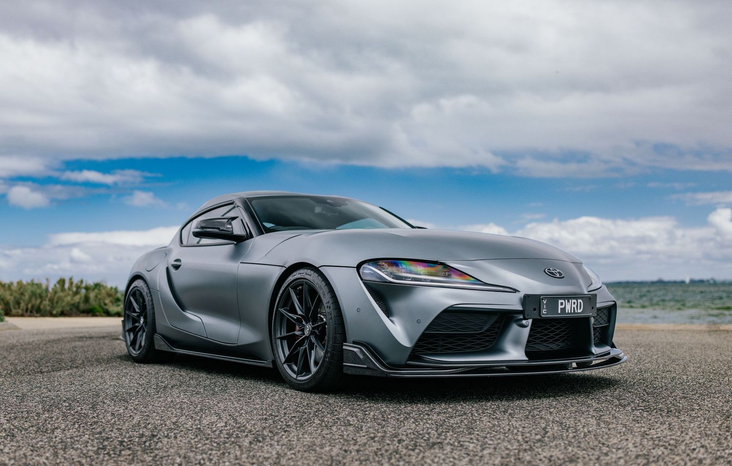 Silver Toyota GR Supra with black wheels and body kit on an open tarmac.
