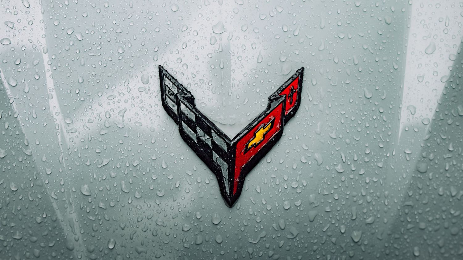 Corvette crossed flags emblem badge on a wet silver car hood covered in raindrops.