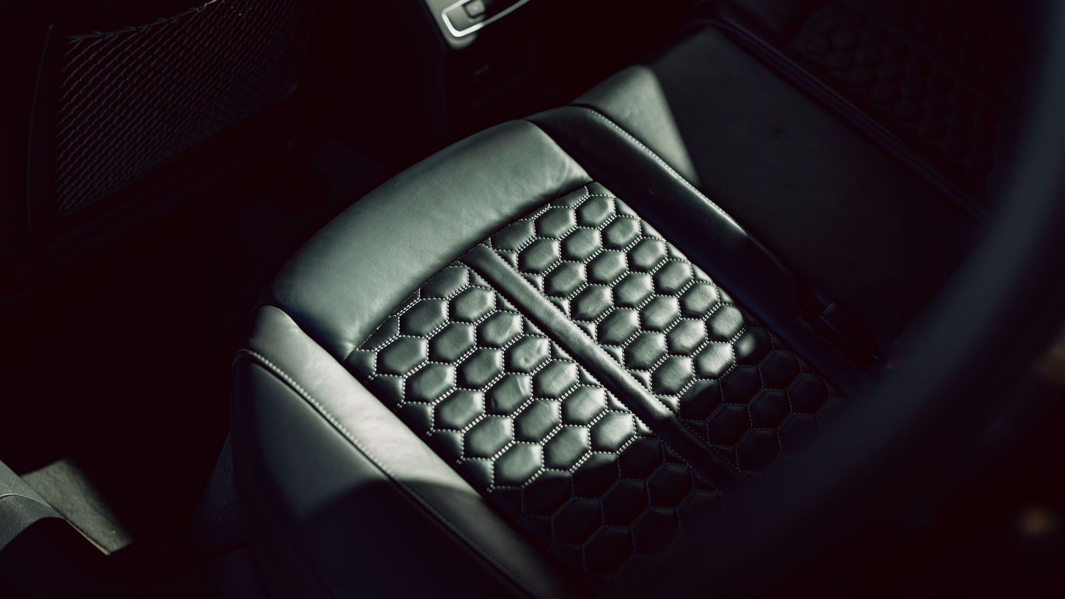 Close-up of a hexagonal pattern car seat cushion insert in a dark leather vehicle interior.