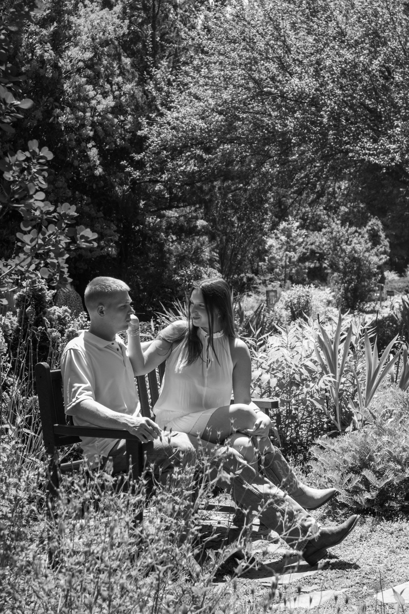 Black and white photo of a couple sitting together in a lush garden, sharing an intimate moment.
