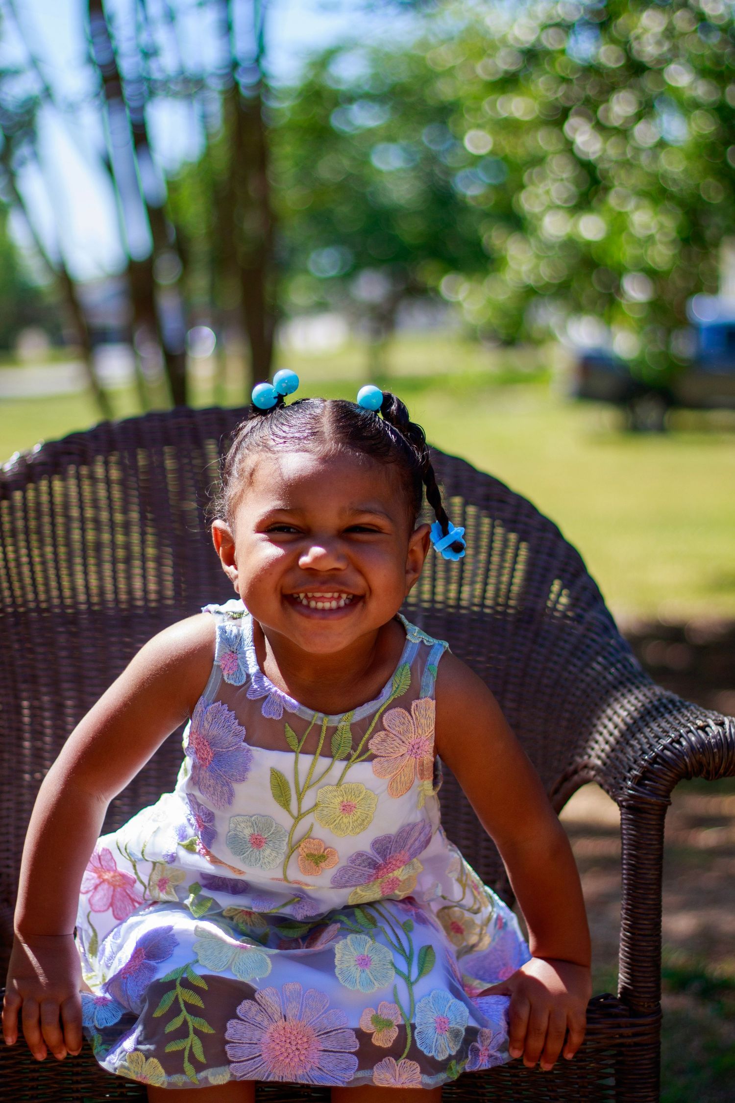 Happy toddler girl in floral dress sitting in wicker chair outdoors.