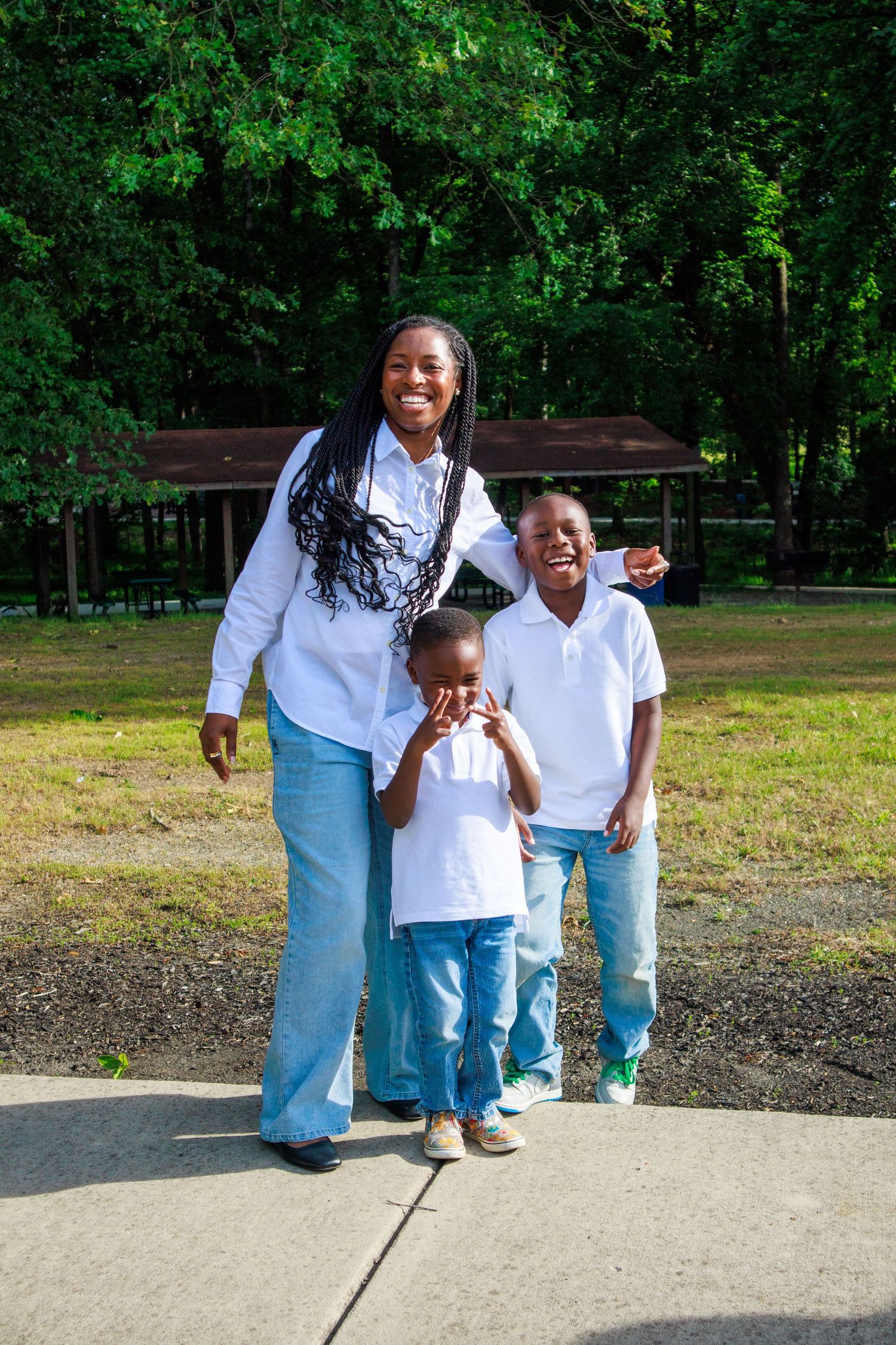 A joyful mother and two children pose together in a park, wearing matching white shirts and blue jeans.