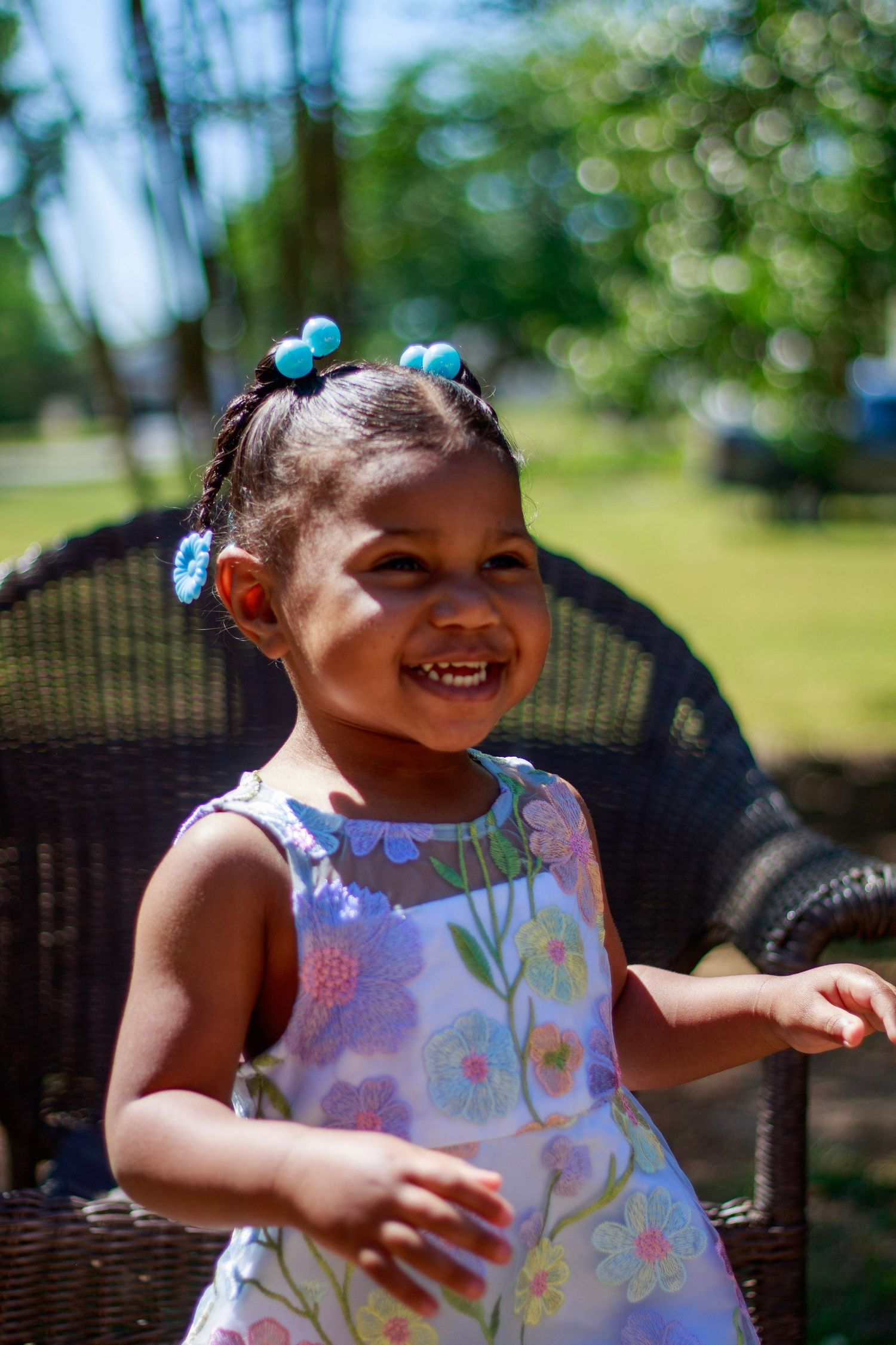 Smiling toddler girl in floral dress with blue hair accessories outdoors.