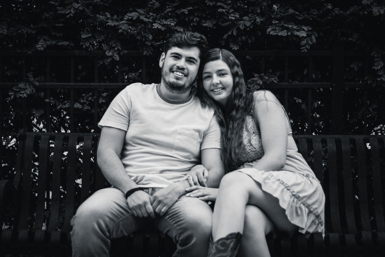 A black and white portrait of a smiling couple sitting closely together on a bench outdoors.