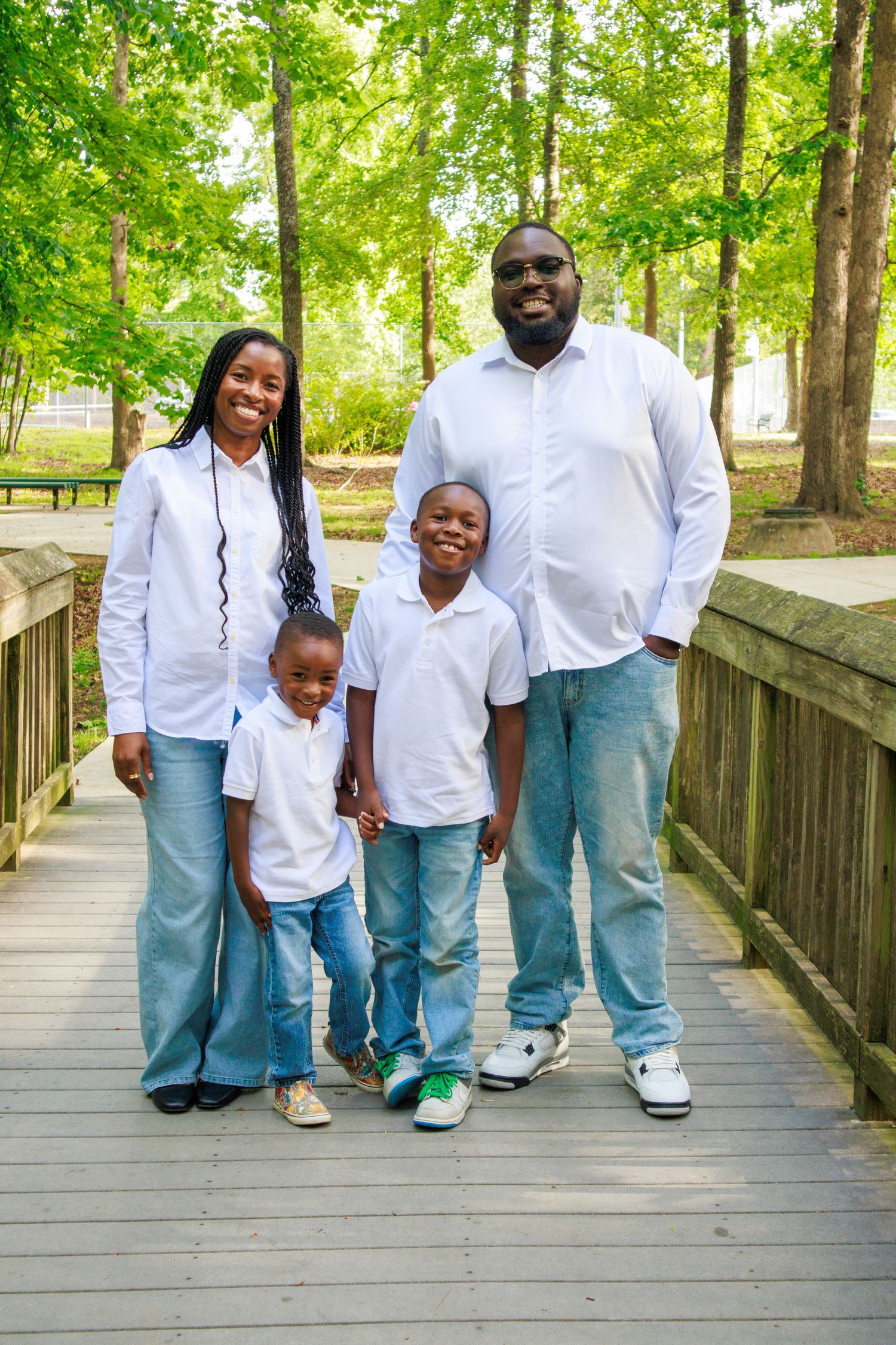 Happy African American family of four in matching white shirts and jeans posing on a wooden bridge in a park.