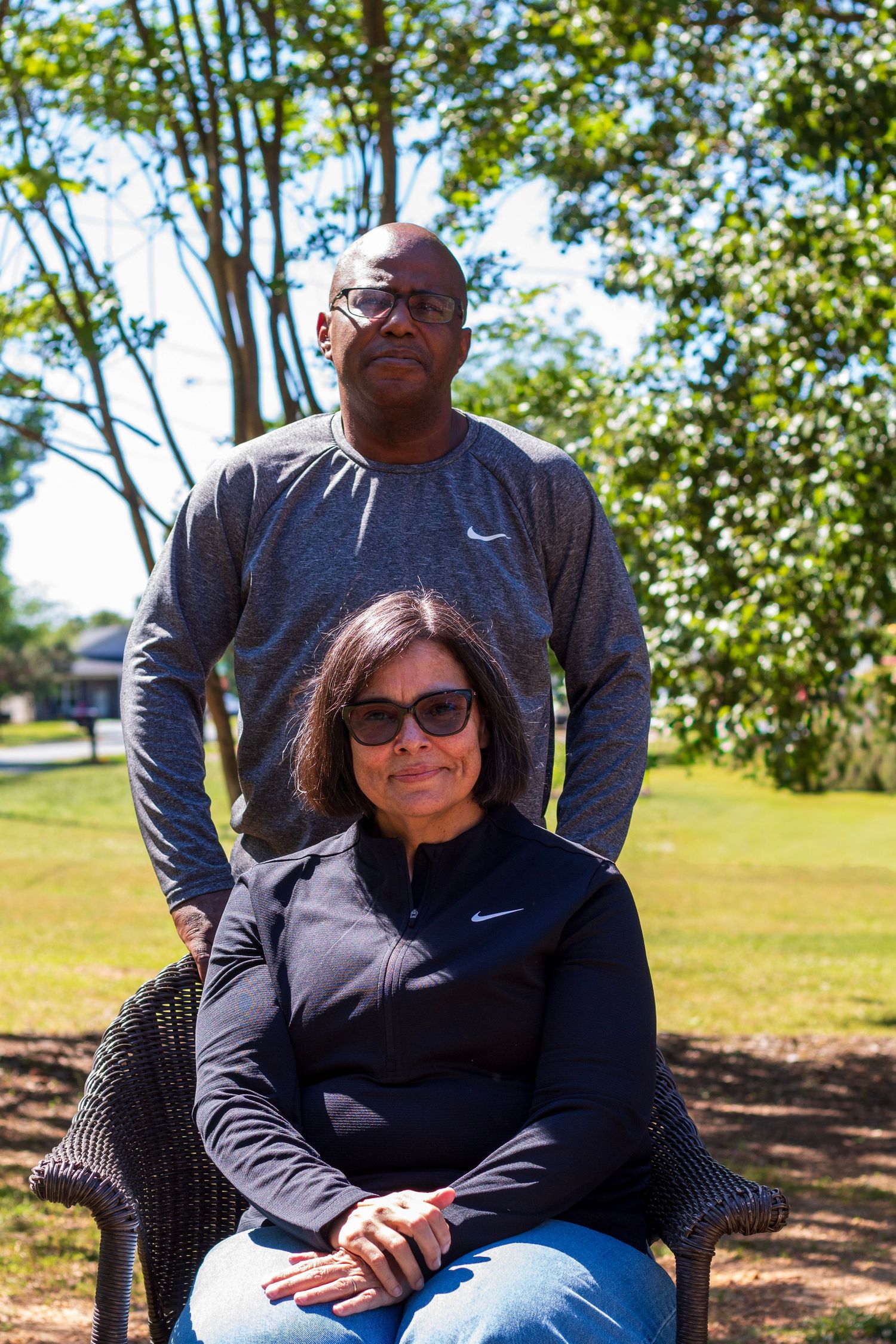 A man and woman posing outdoors in a park, both wearing Nike athletic wear, with lush green trees in the background.