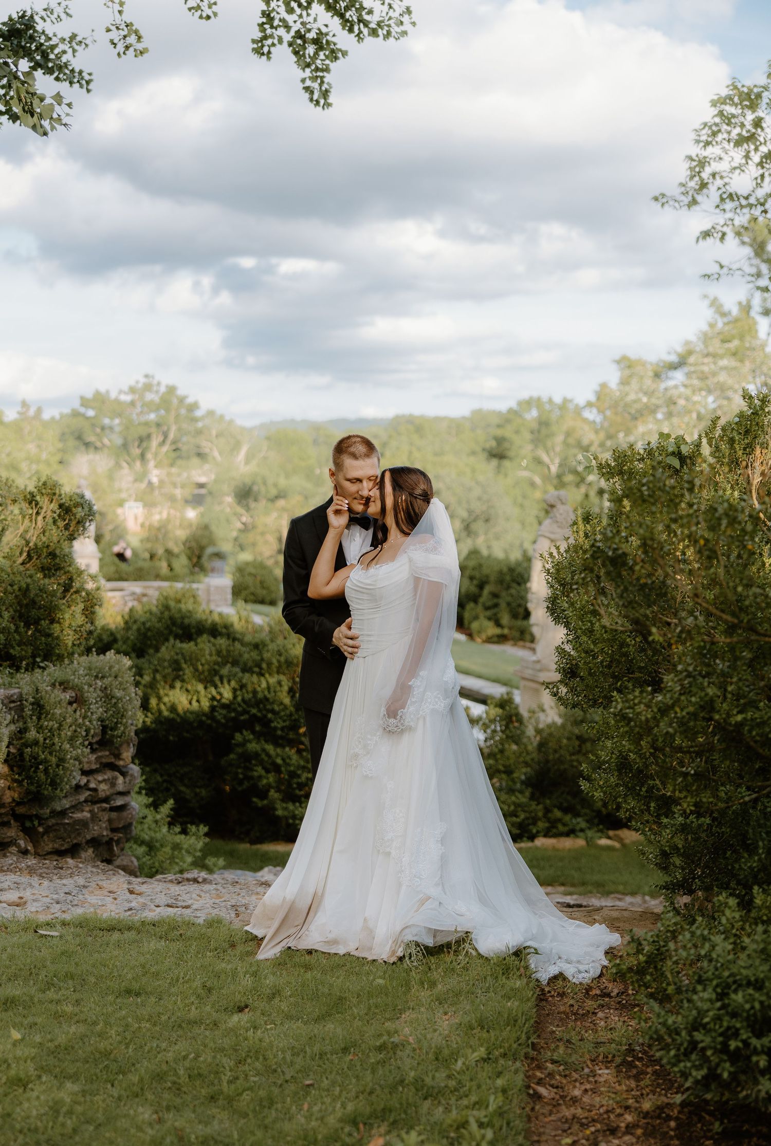 Bride and groom share a romantic embrace in a lush garden setting, bride wearing a flowing white gown with veil.