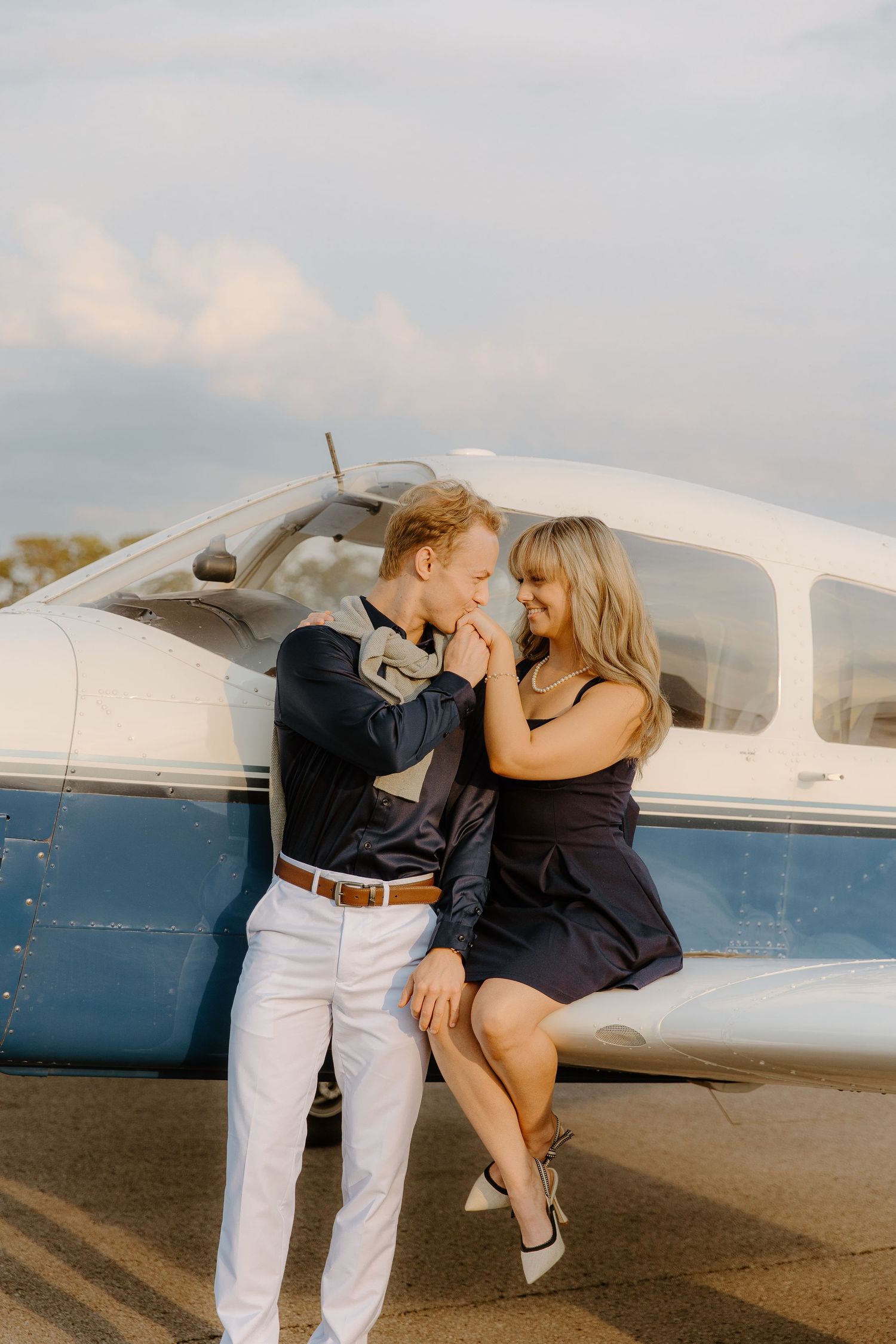 Couple sharing a romantic moment beside a small aircraft at sunset.