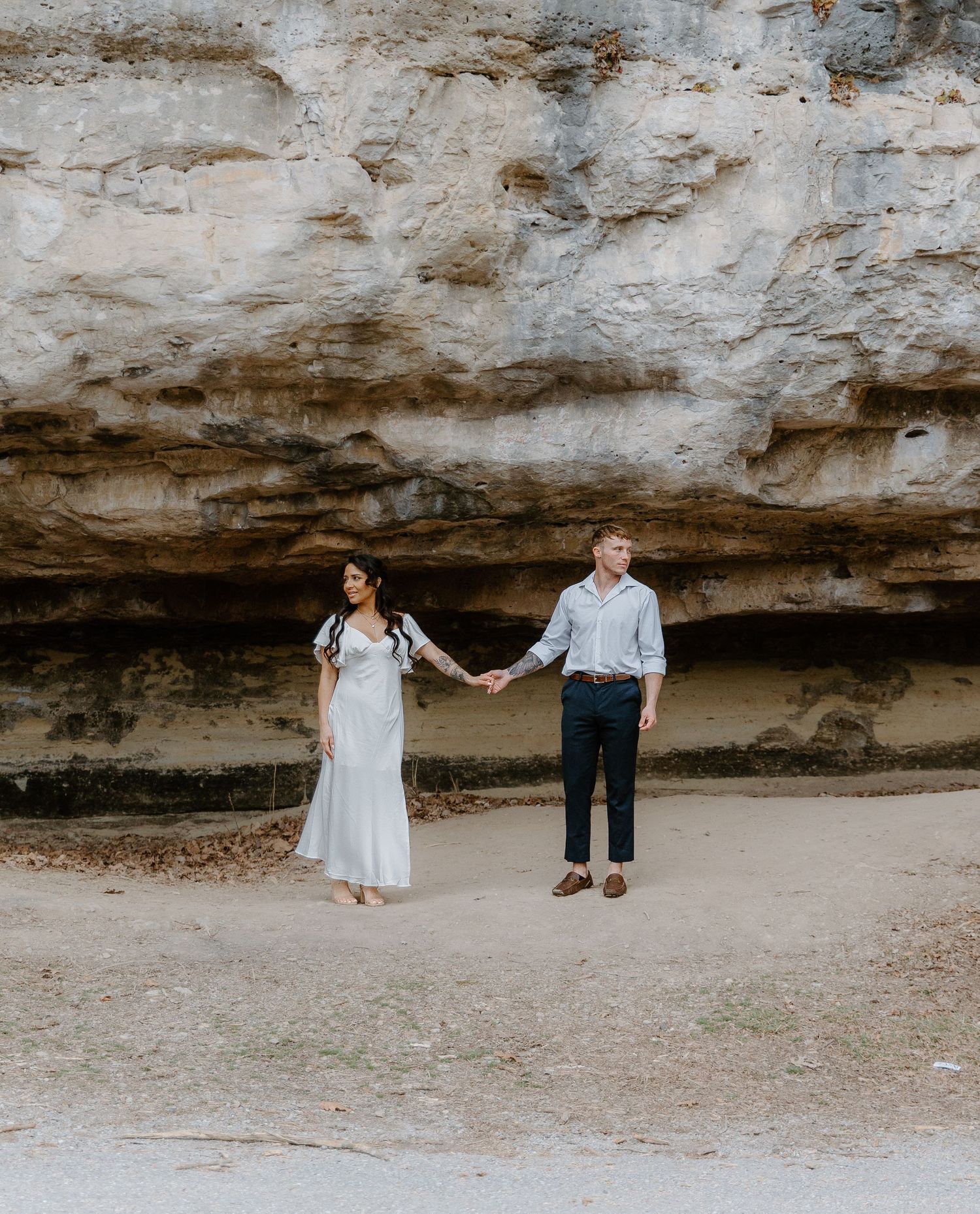 Couple holds hands near a sandy cliff during an outdoor engagement photo session.