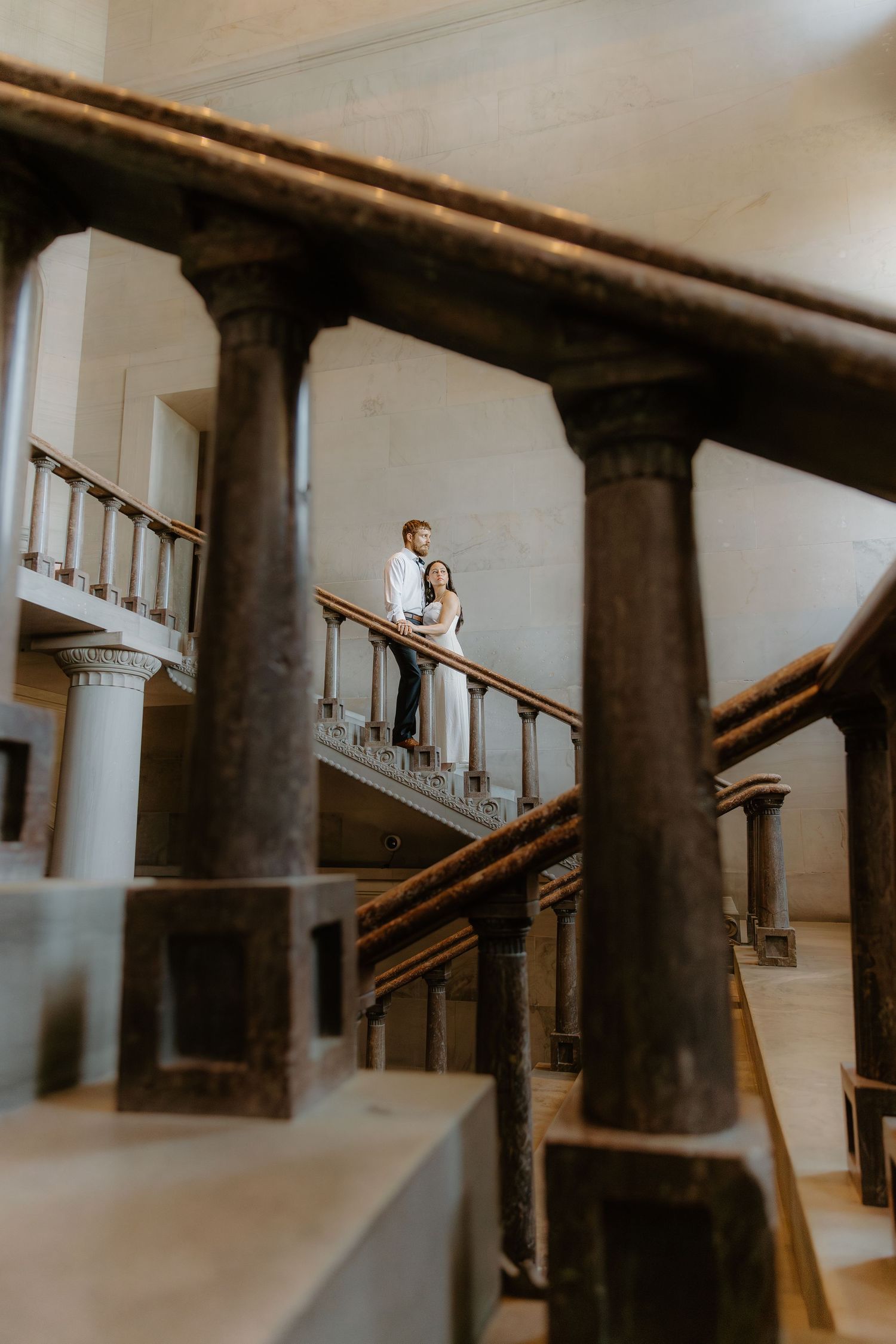 Couple embracing on ornate balcony with classical columns in elegant historic building interior.