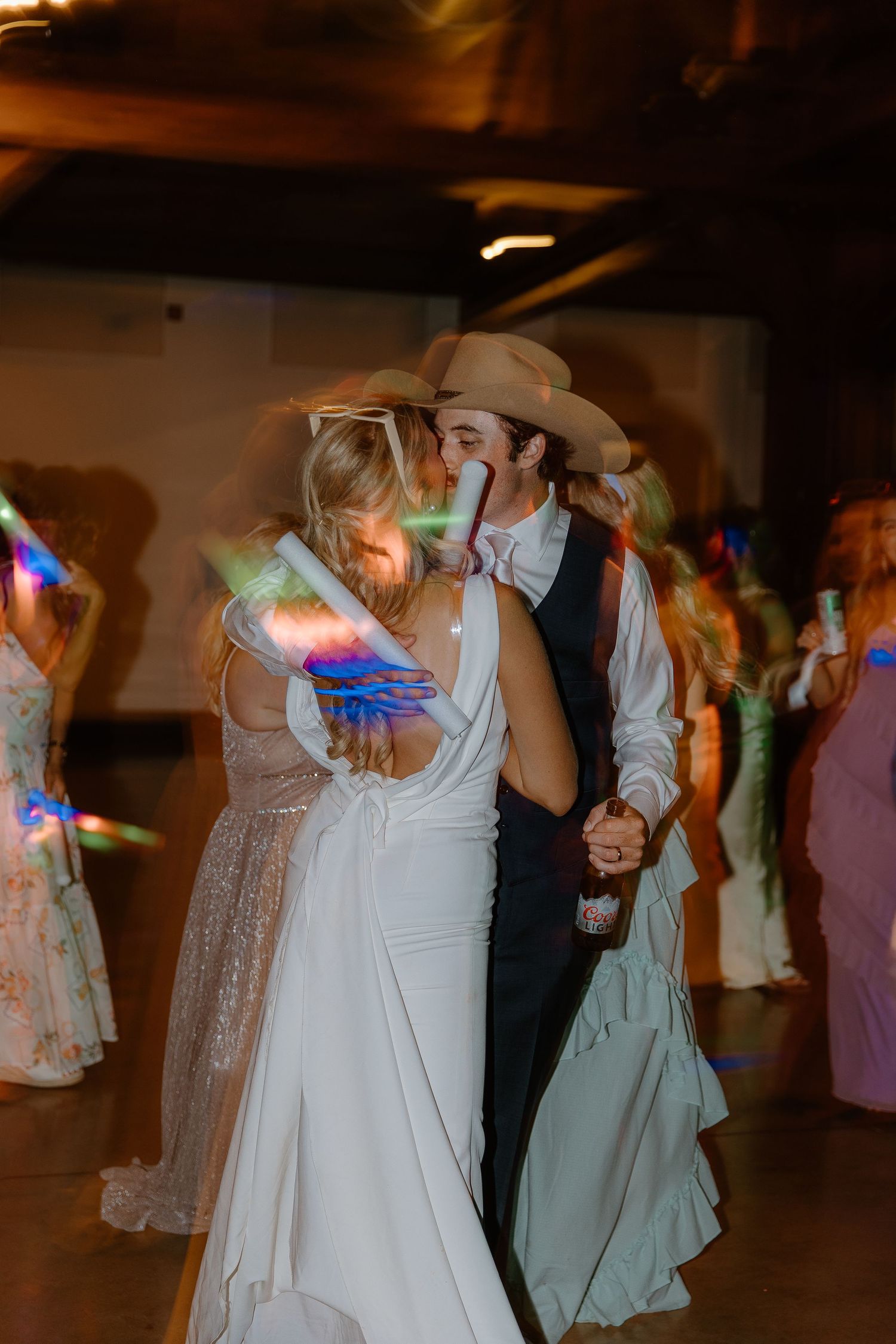 Bride and groom kiss on the dance floor surrounded by colorful glow sticks at their wedding reception.