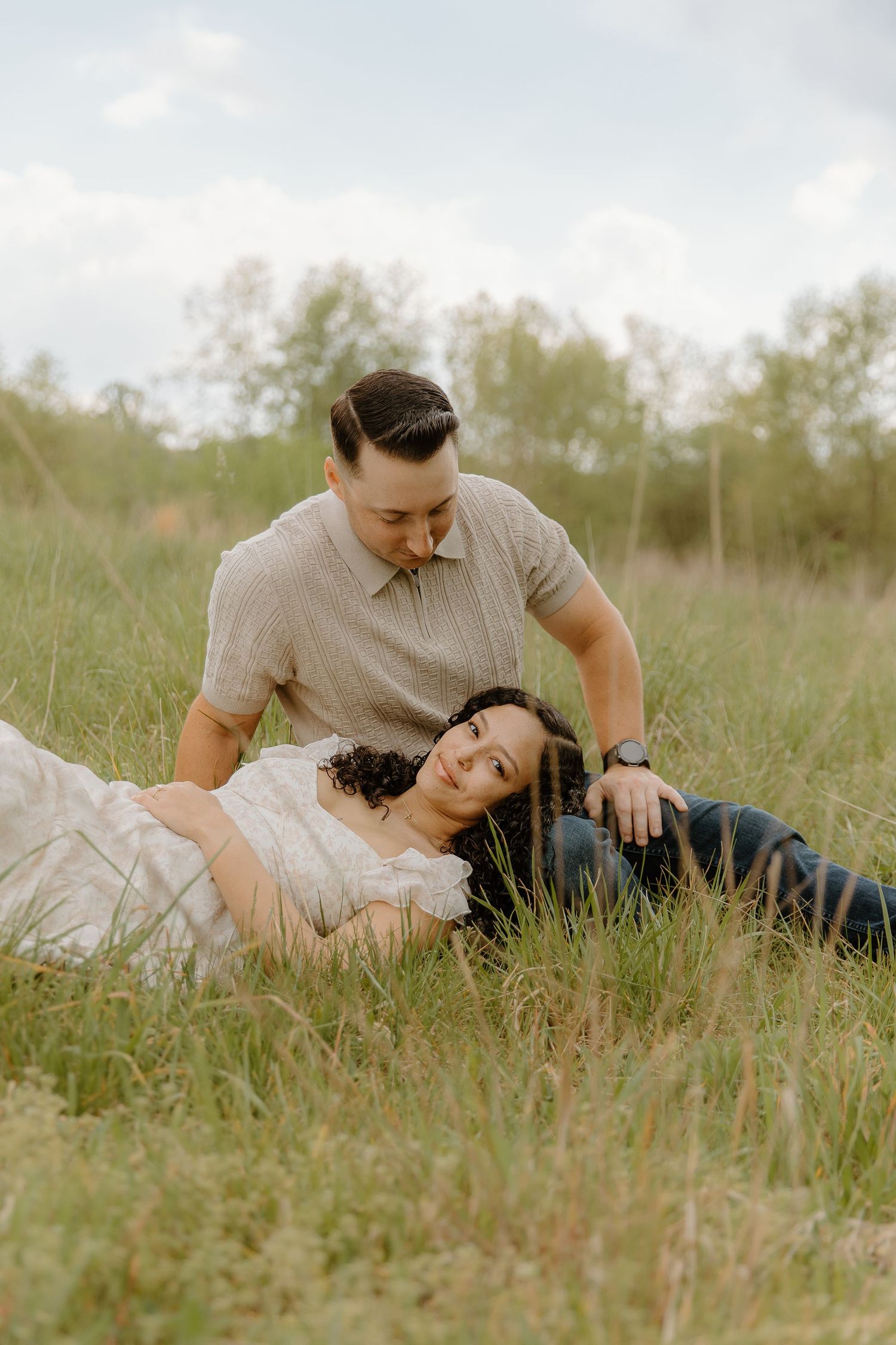 Couple relaxing together in a grassy field under a cloudy sky.