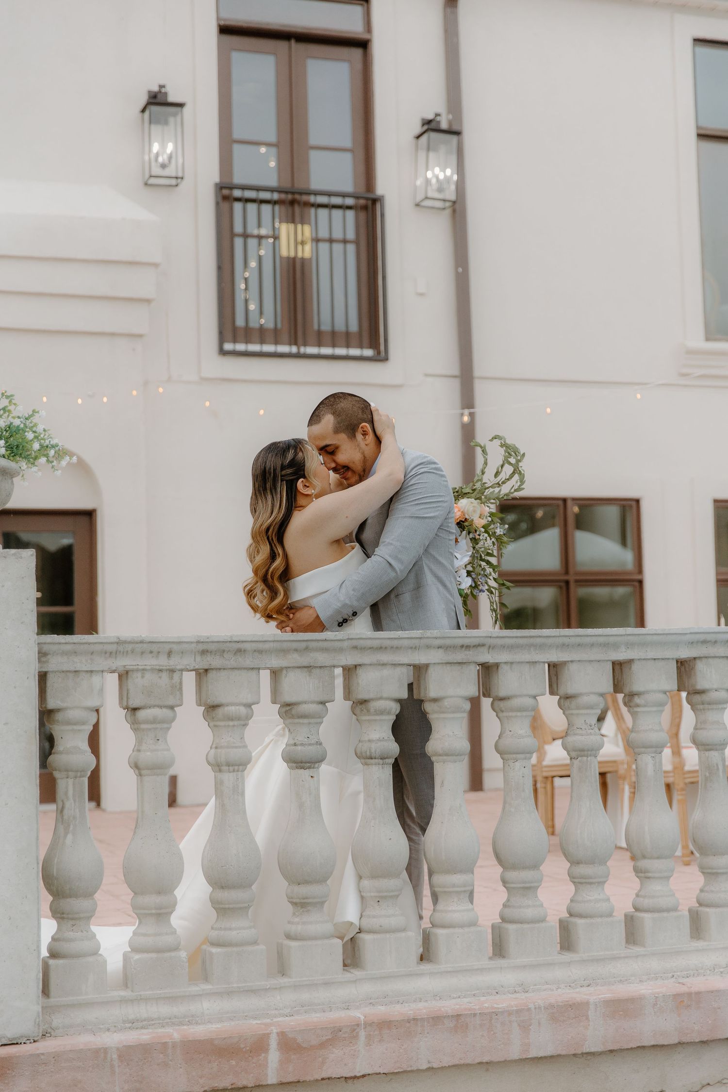 Bride and groom sharing a romantic kiss on an elegant white balustrade terrace outside a classic venue.