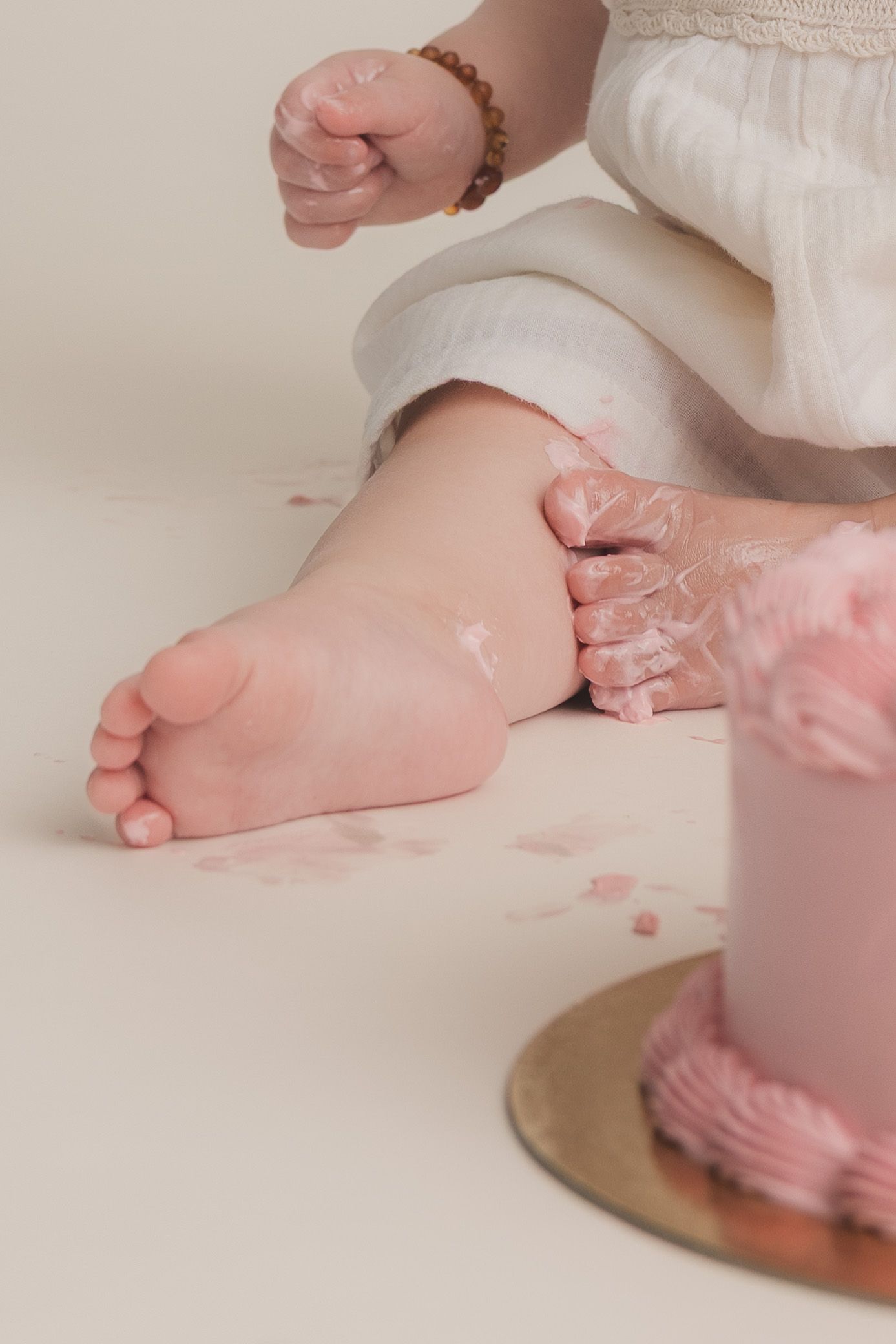 Baby feet covered in pink frosting next to a smash cake during a first birthday photo session.