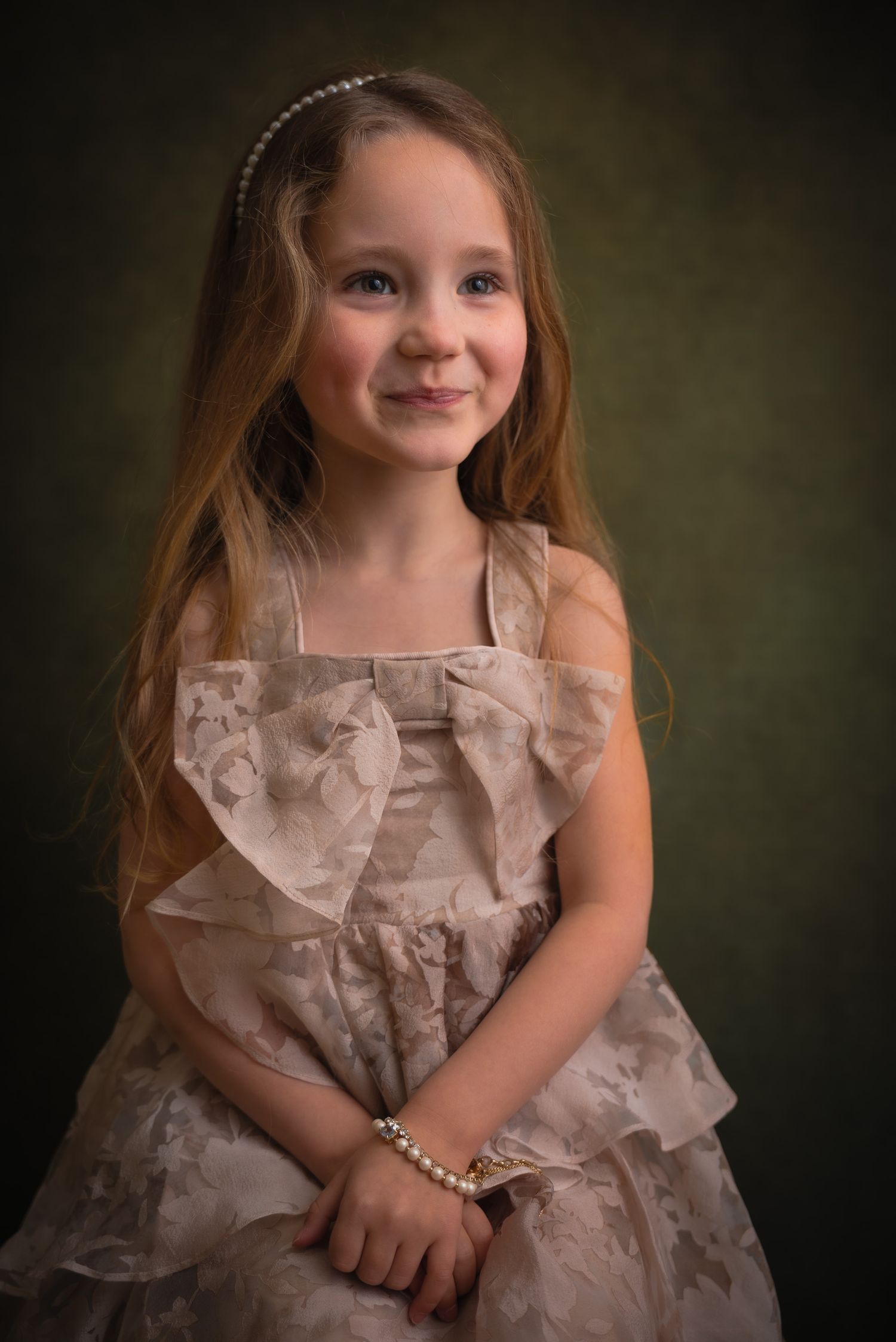Young girl in elegant lace dress with pearl bracelet and headband smiling for a studio portrait photo.