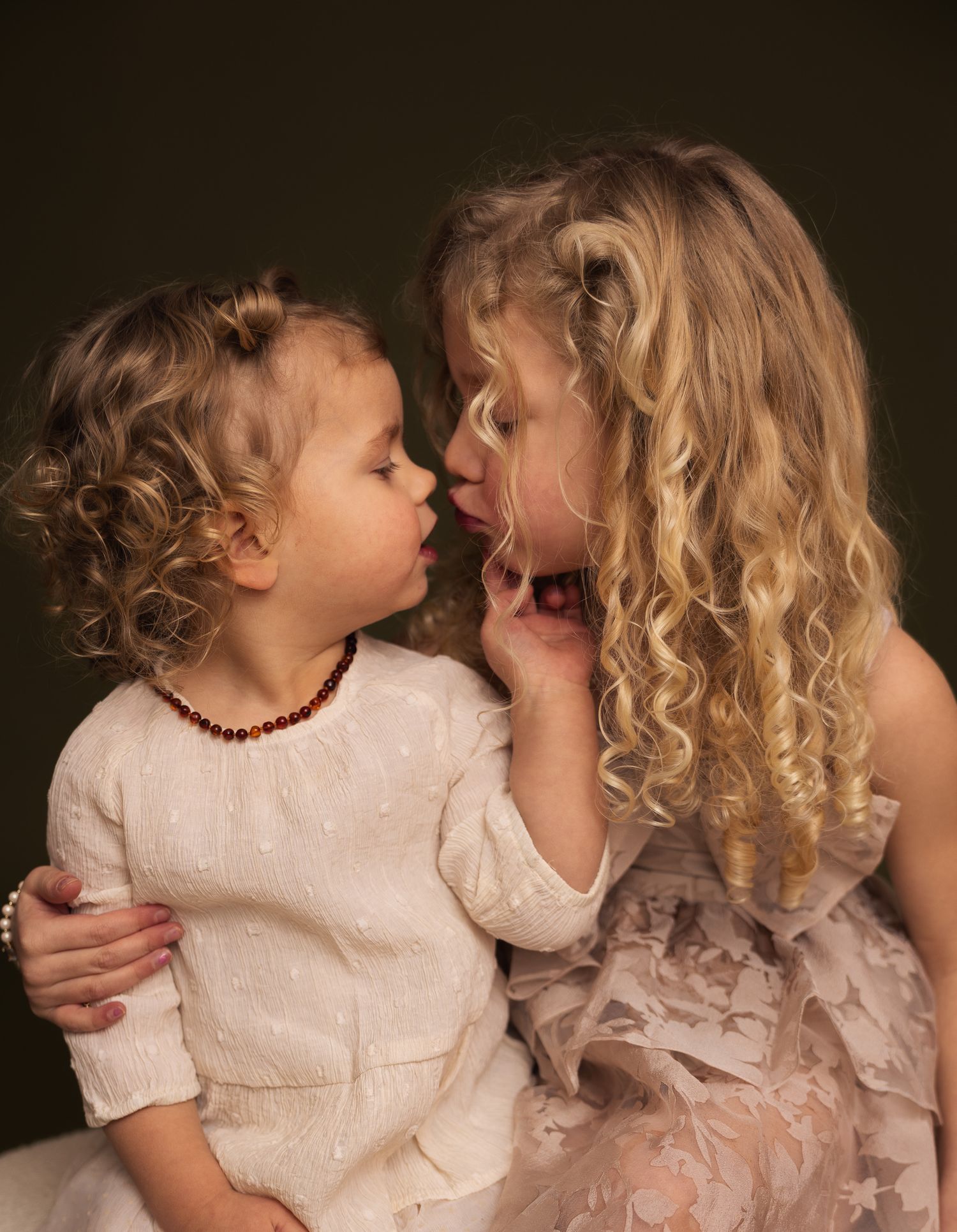 Lief kinderportret van twee zusjes die elkaar een kus geven in de fotostudio.